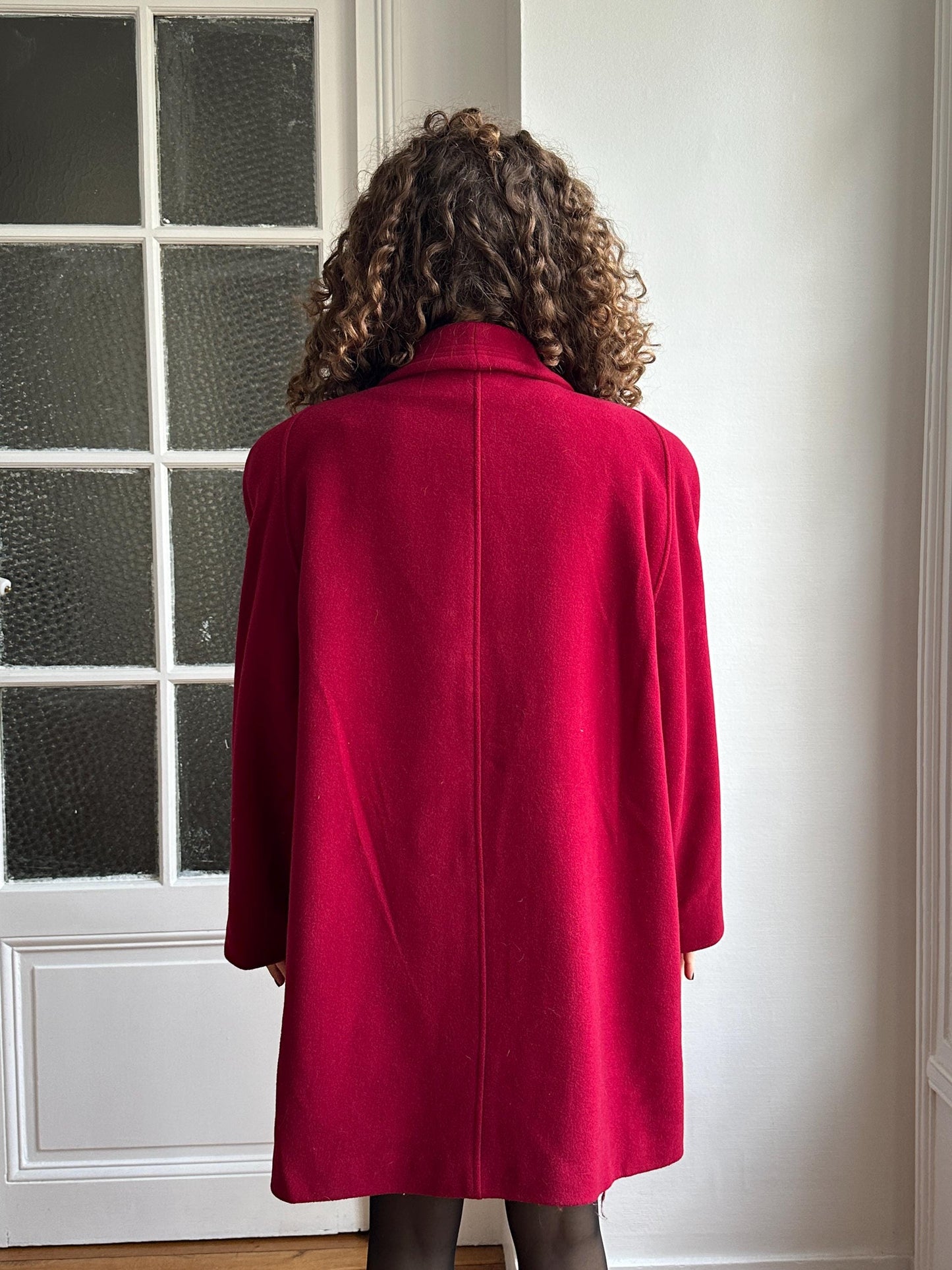 A person wearing a red coat is standing in front of a white door.