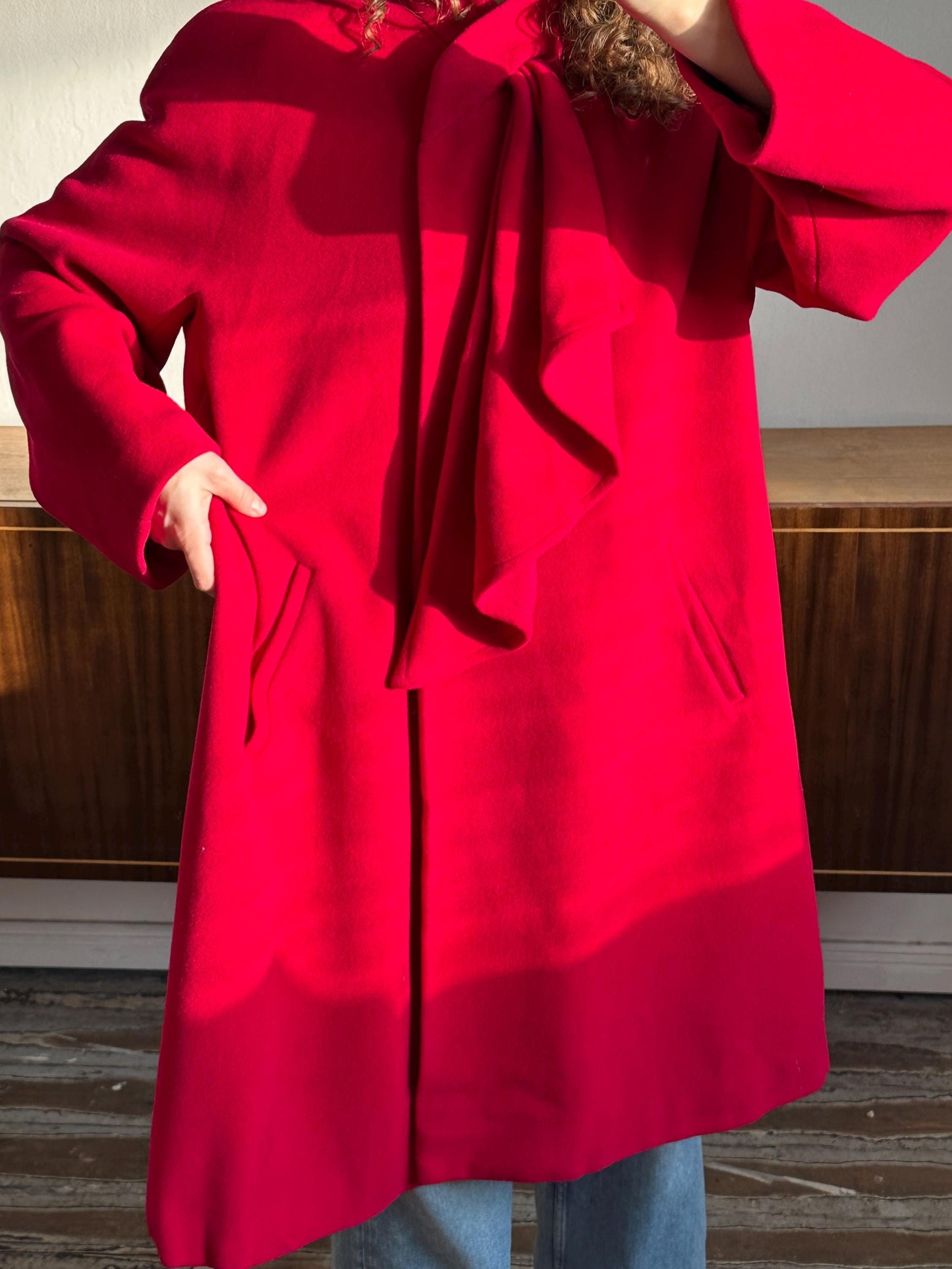 A person wearing a bright red coat with a ruffled collar and a large pocket.