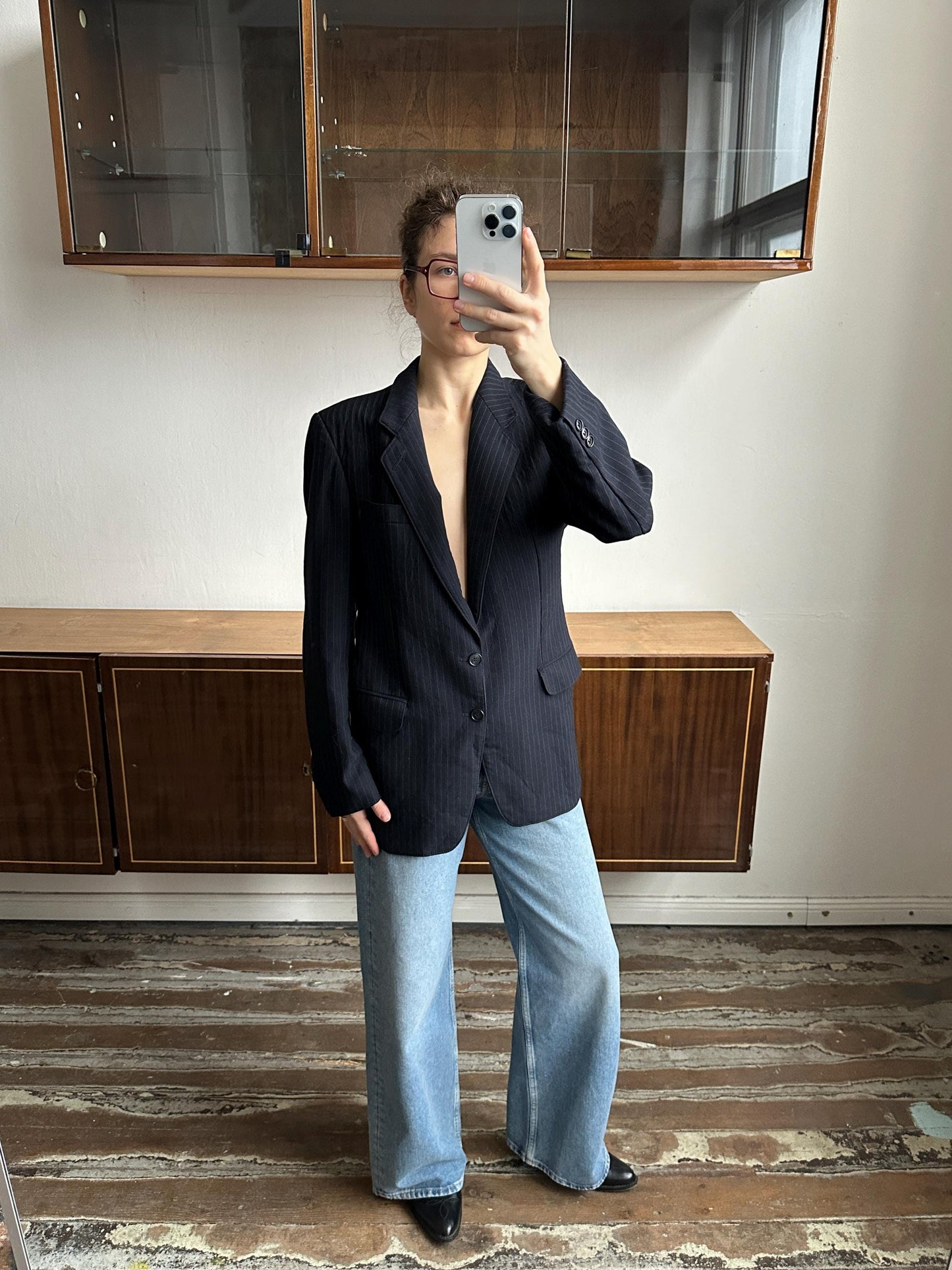A person is taking a selfie in a room with a wooden floor and a glass cabinet.
