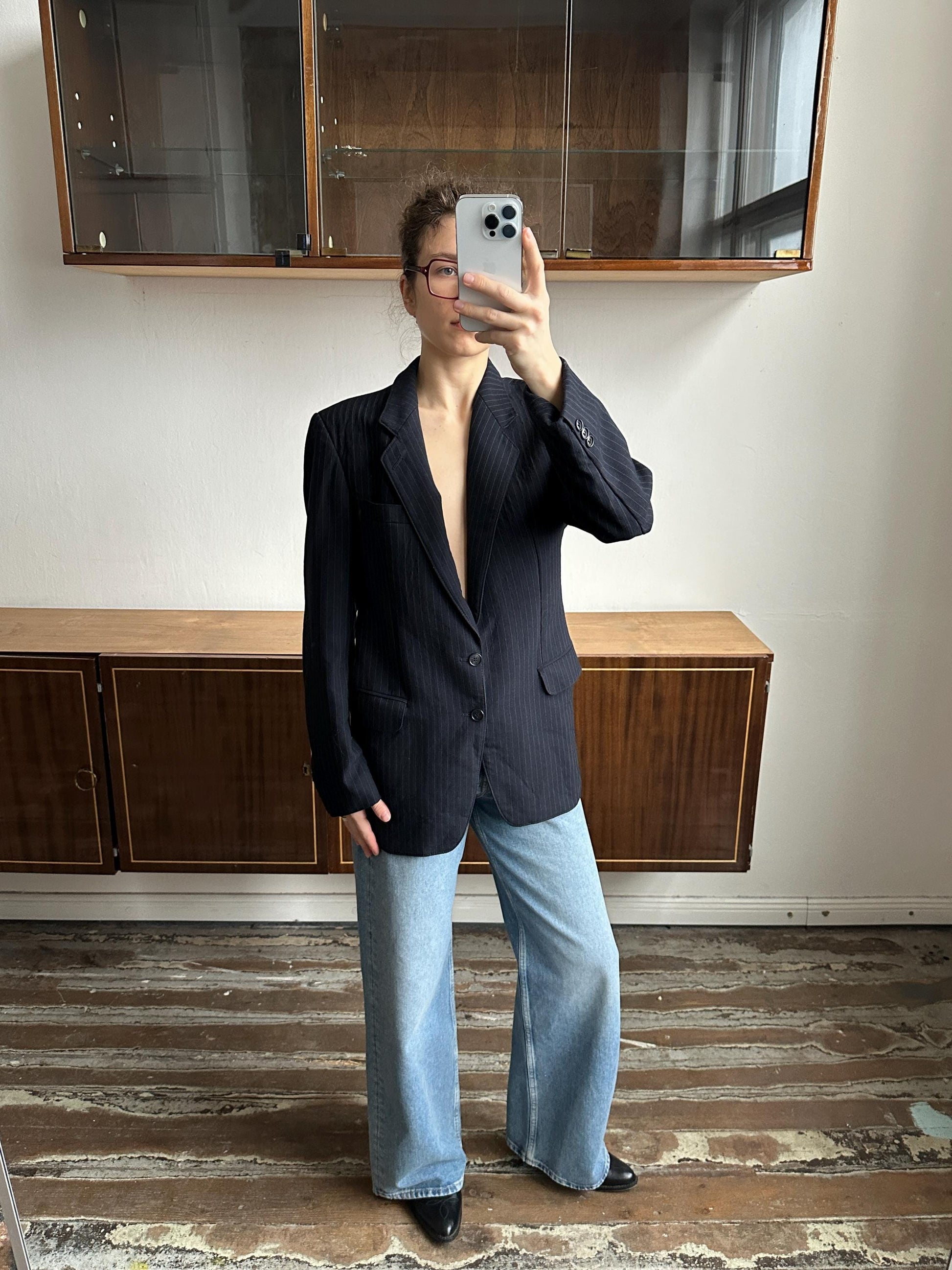 A person is taking a selfie in a room with a wooden floor and a glass cabinet.
