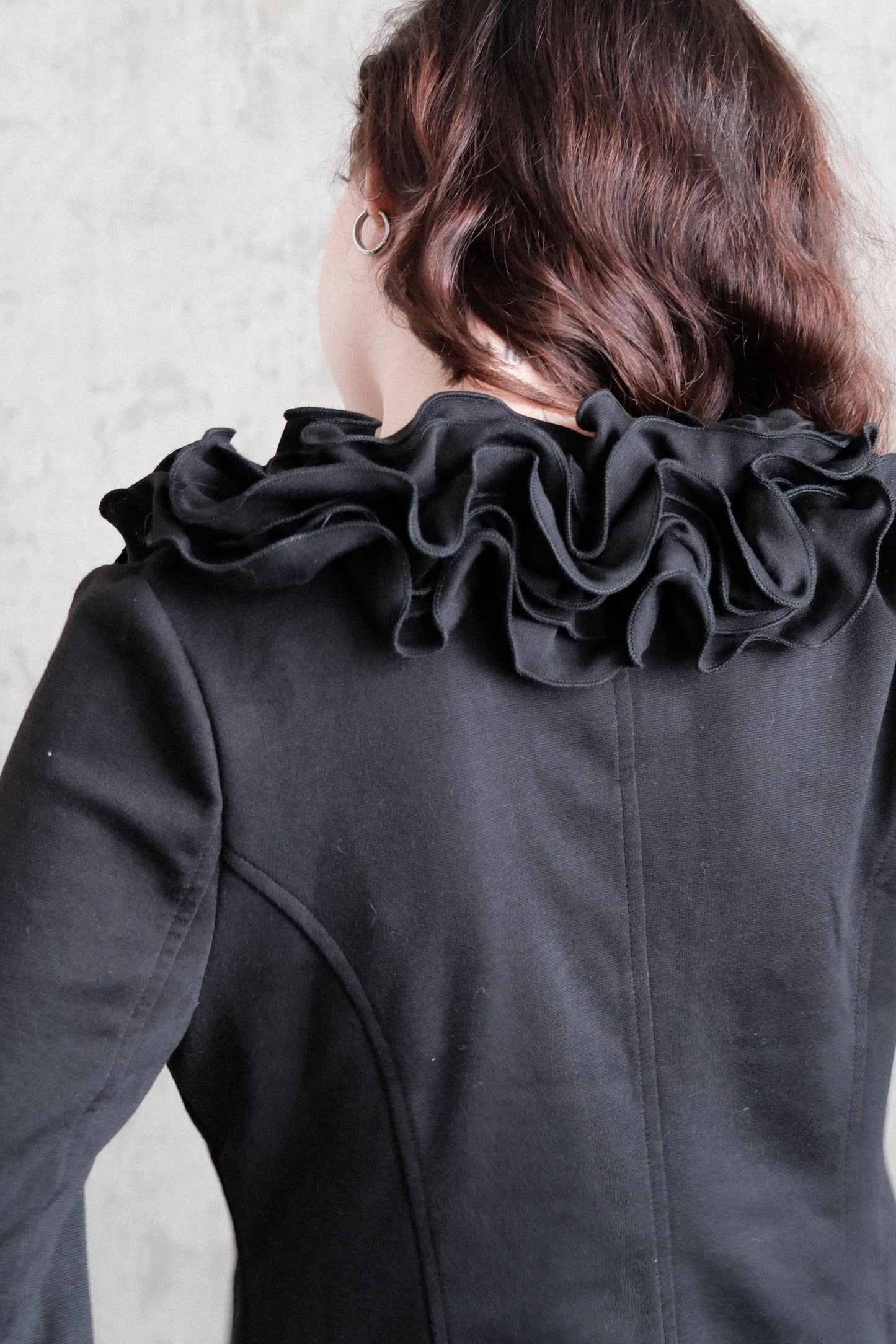a close-up view of a person's back, wearing a black jacket with ruffled details.