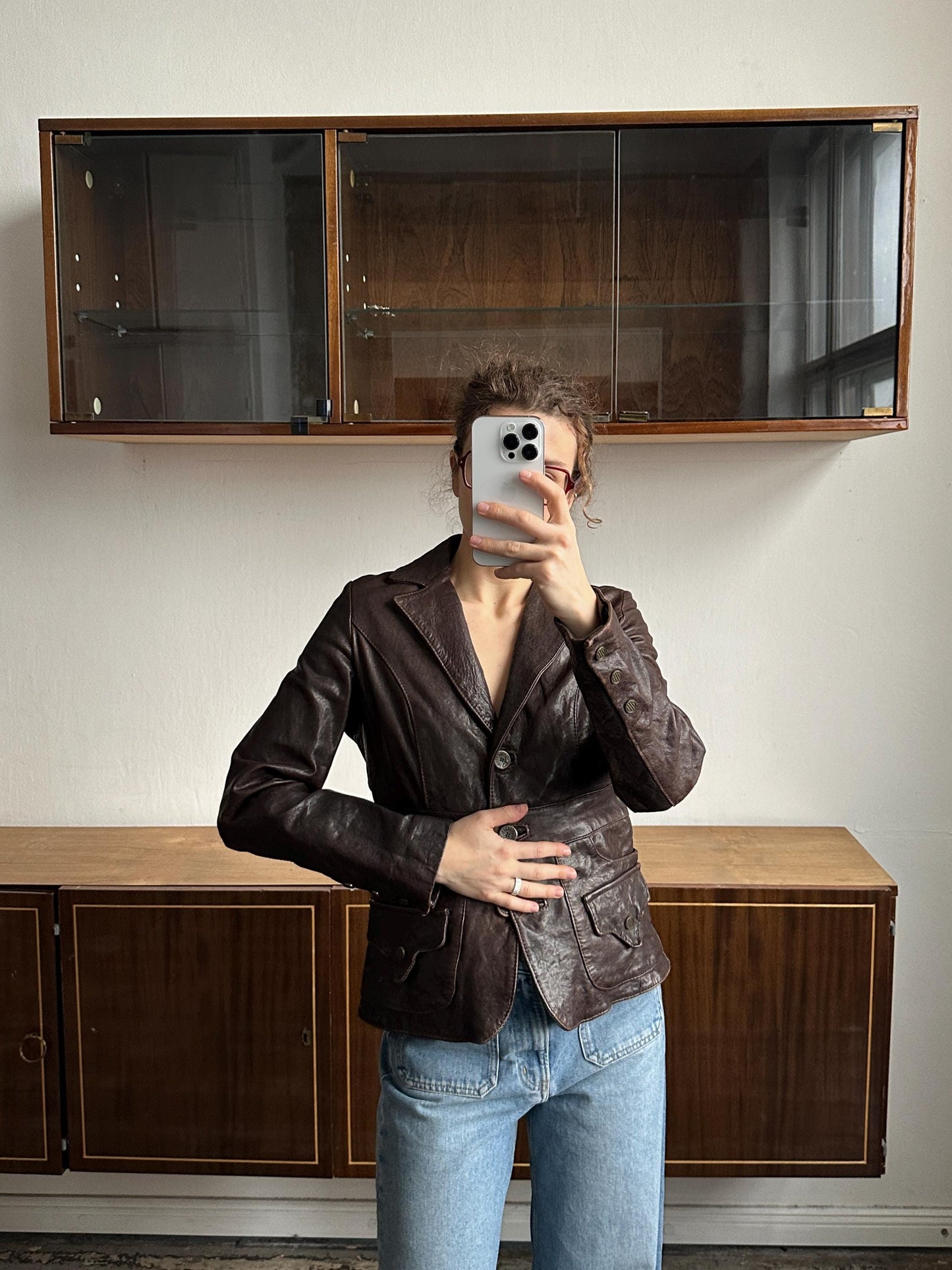 A person is taking a selfie with a smartphone in front of a wooden cabinet.