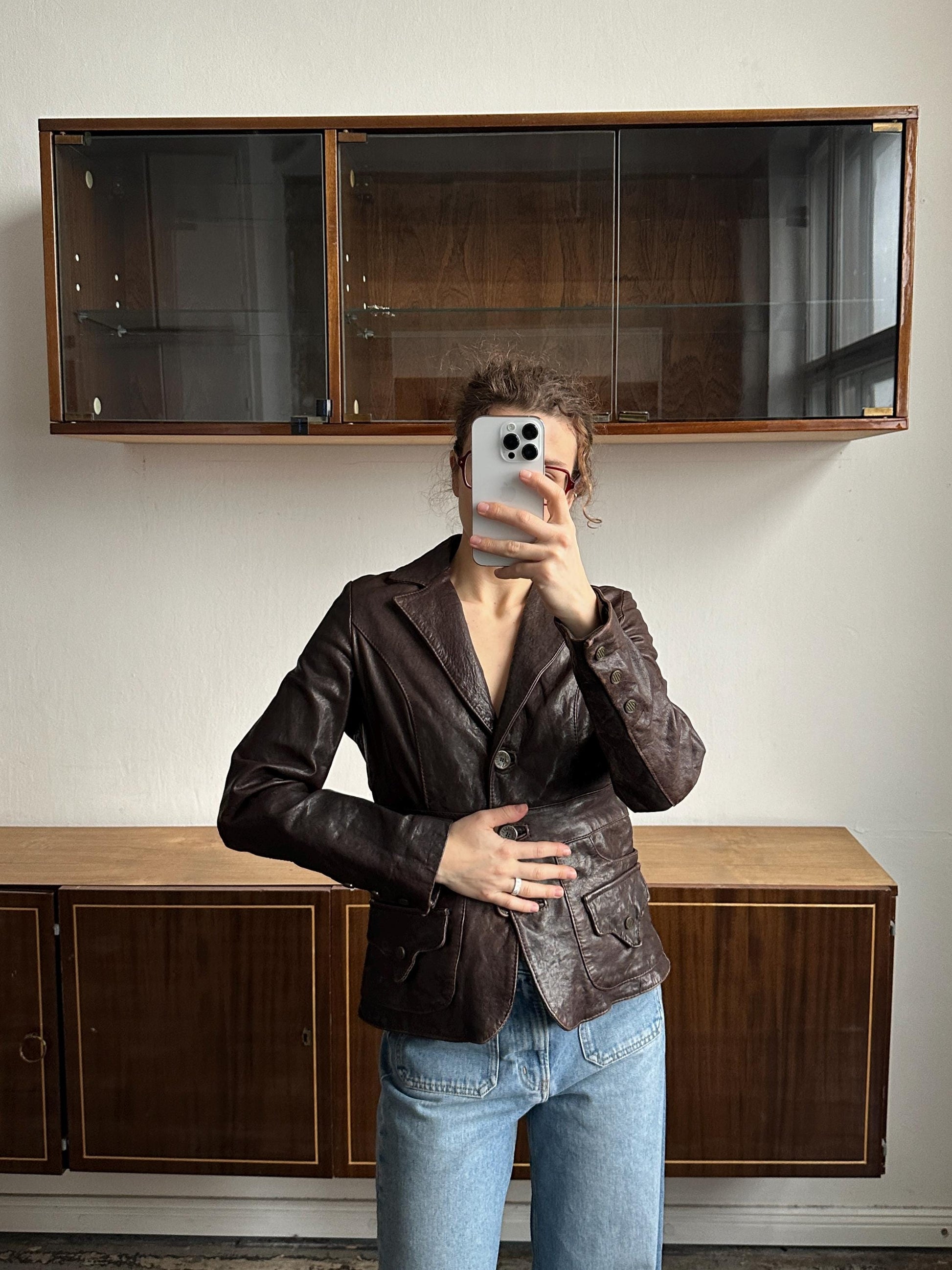 A person is taking a selfie with a smartphone in front of a wooden cabinet.