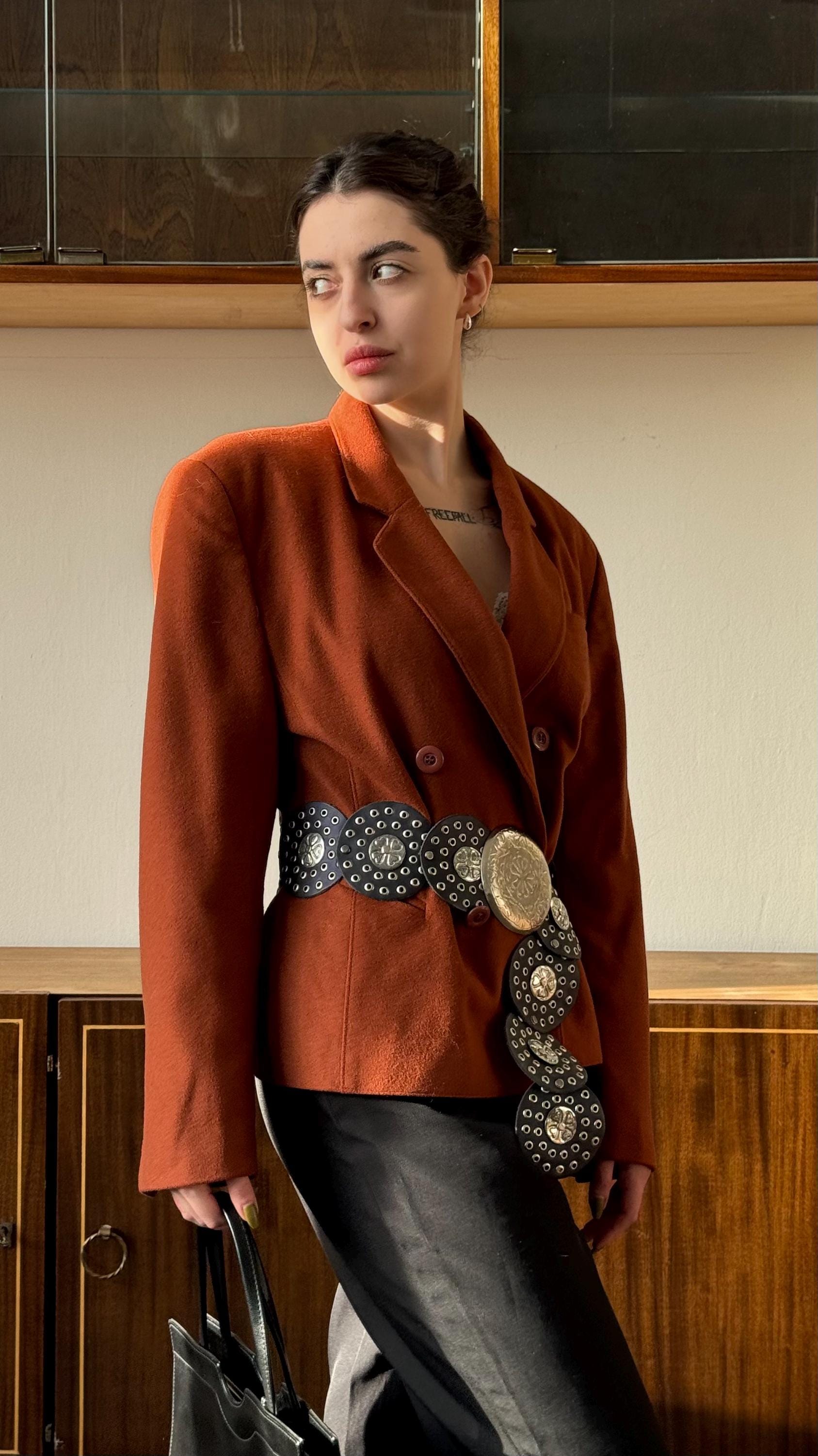 A woman wearing a brown blazer and carrying a black purse stands in front of a wooden cabinet.