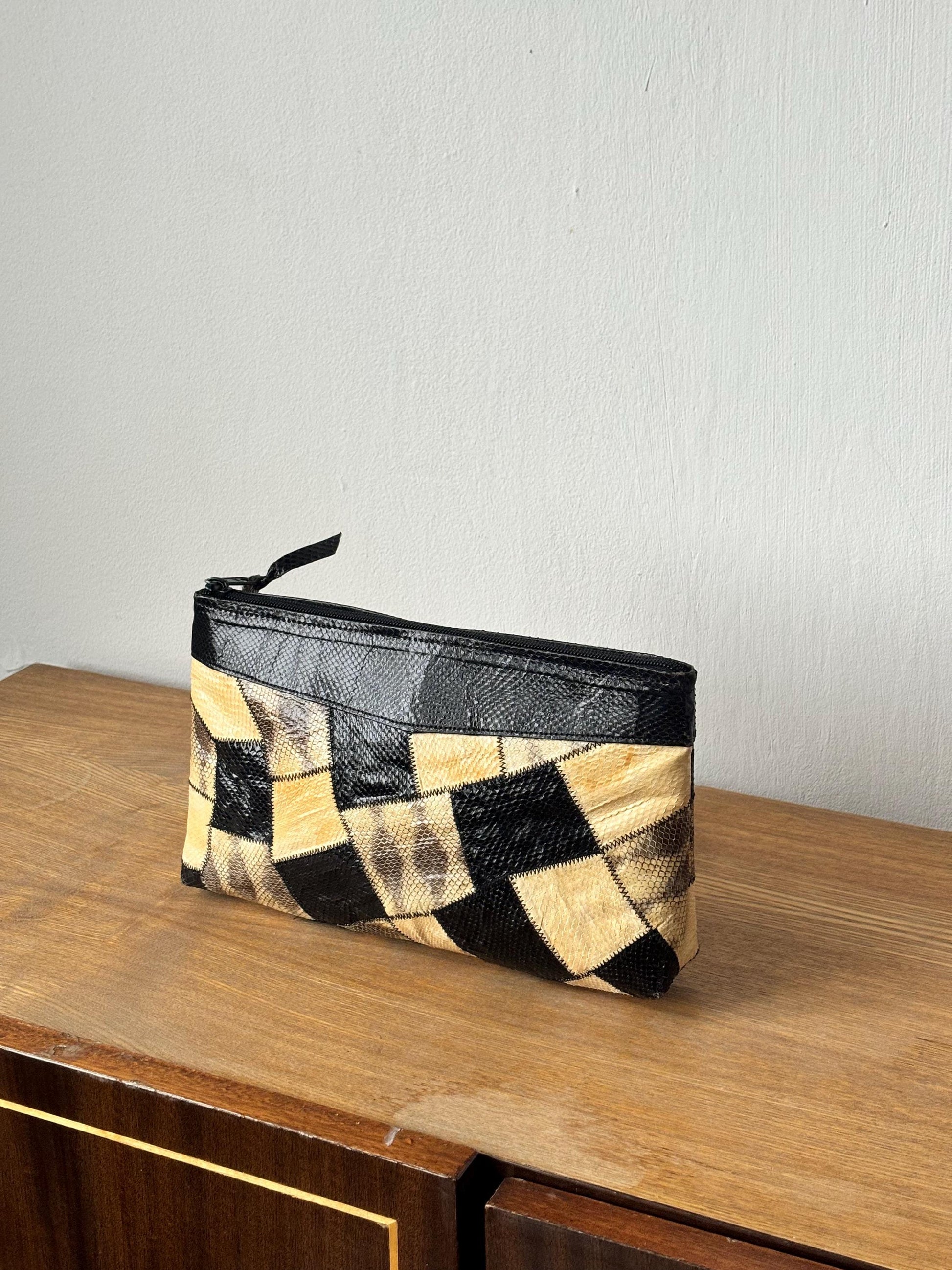 A black and white patterned clutch purse is placed on a wooden surface against a white wall.