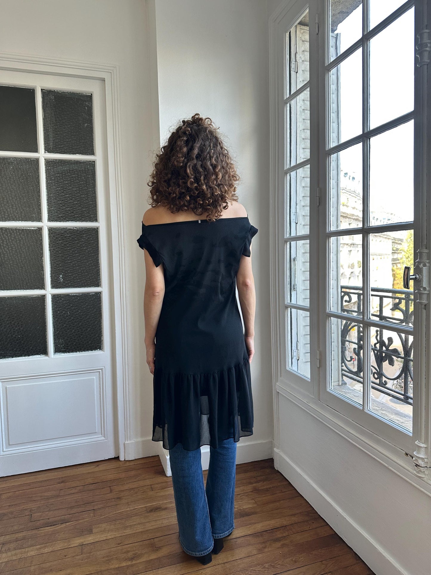 A woman with curly hair is standing in a room, looking out a window.