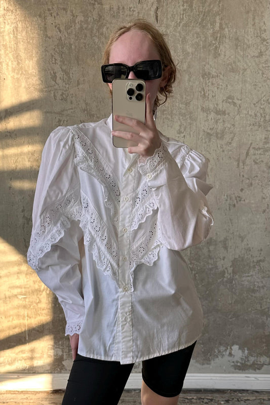 A person is taking a selfie with a smartphone, wearing a white lace blouse and sunglasses.