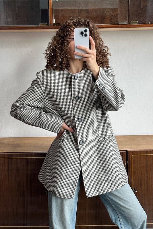 A woman with curly hair is taking a selfie with a smartphone, wearing a black and white checkered jacket and blue jeans.