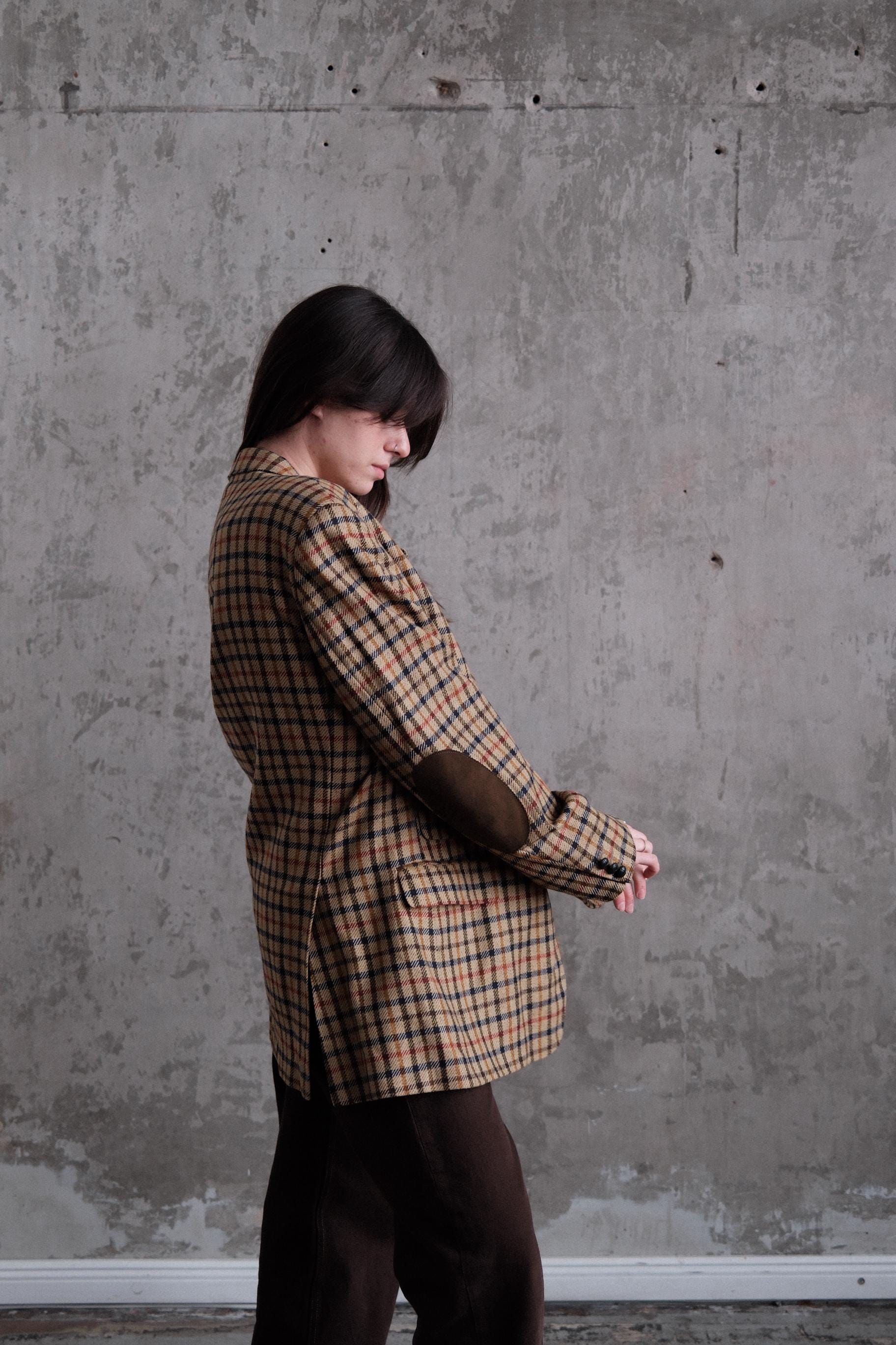 A person wearing a plaid jacket is bending over against a concrete wall.