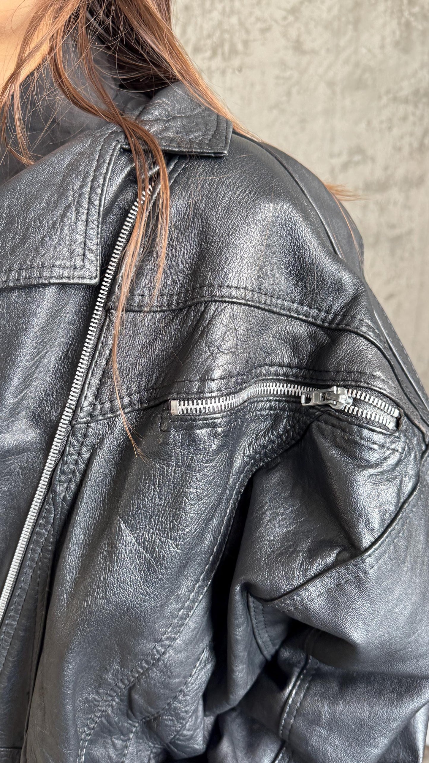 A close-up view of a black leather jacket with a zipper and a pocket.