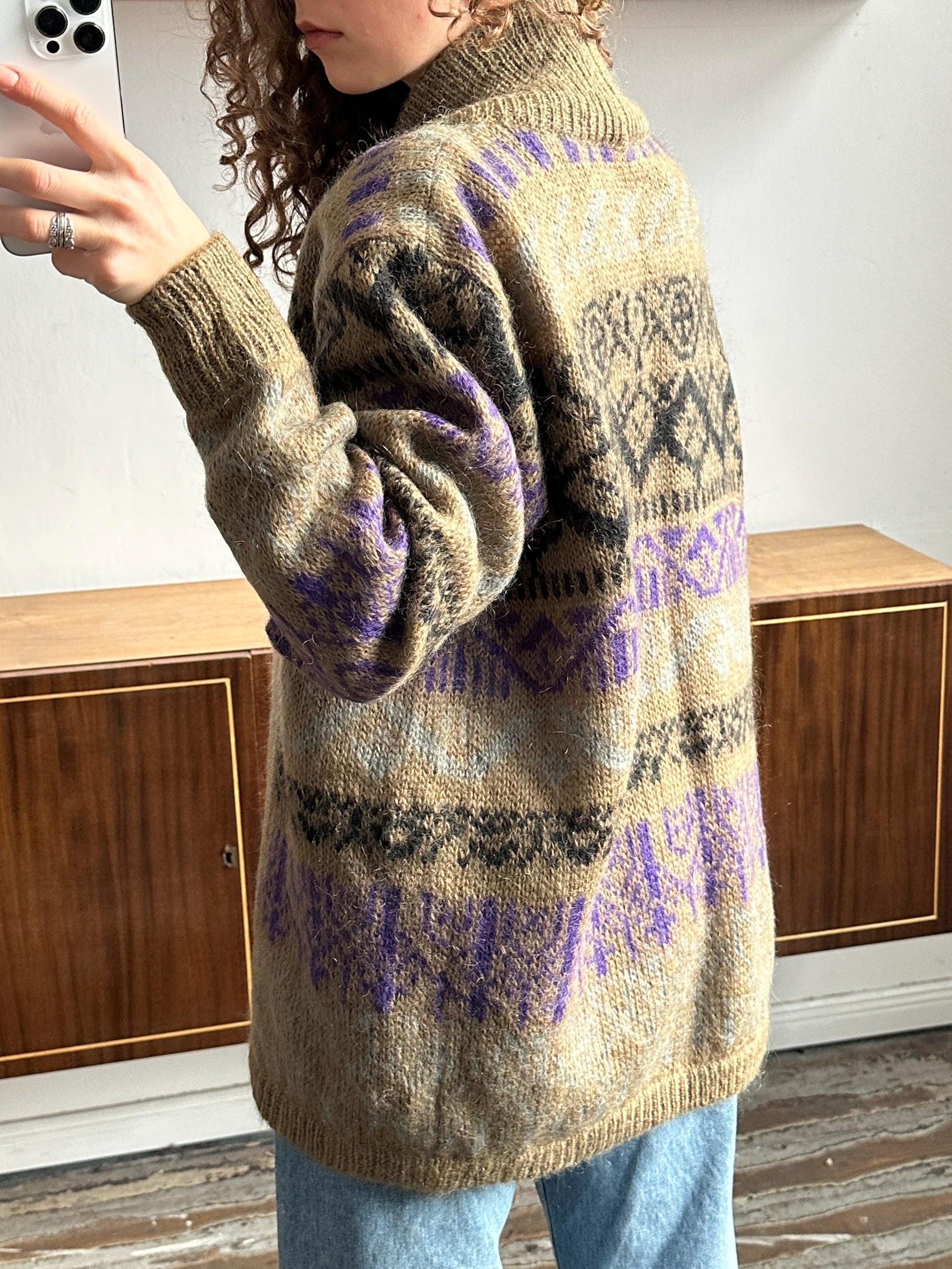 A person wearing a brown and purple patterned sweater stands in front of a wooden cabinet.