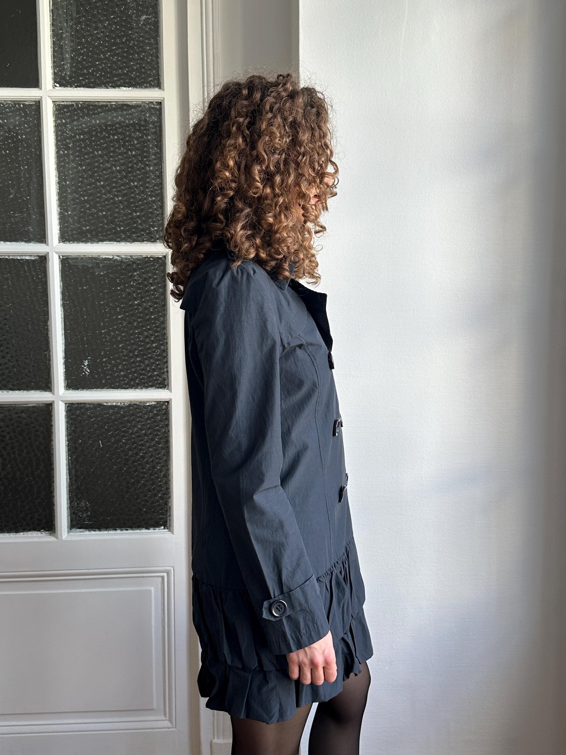 A person with curly hair wearing a black coat is floating in mid-air, with their head turned to the side.