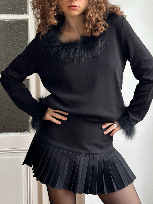 A woman with curly hair wearing a black outfit with a fur collar and a pleated skirt.
