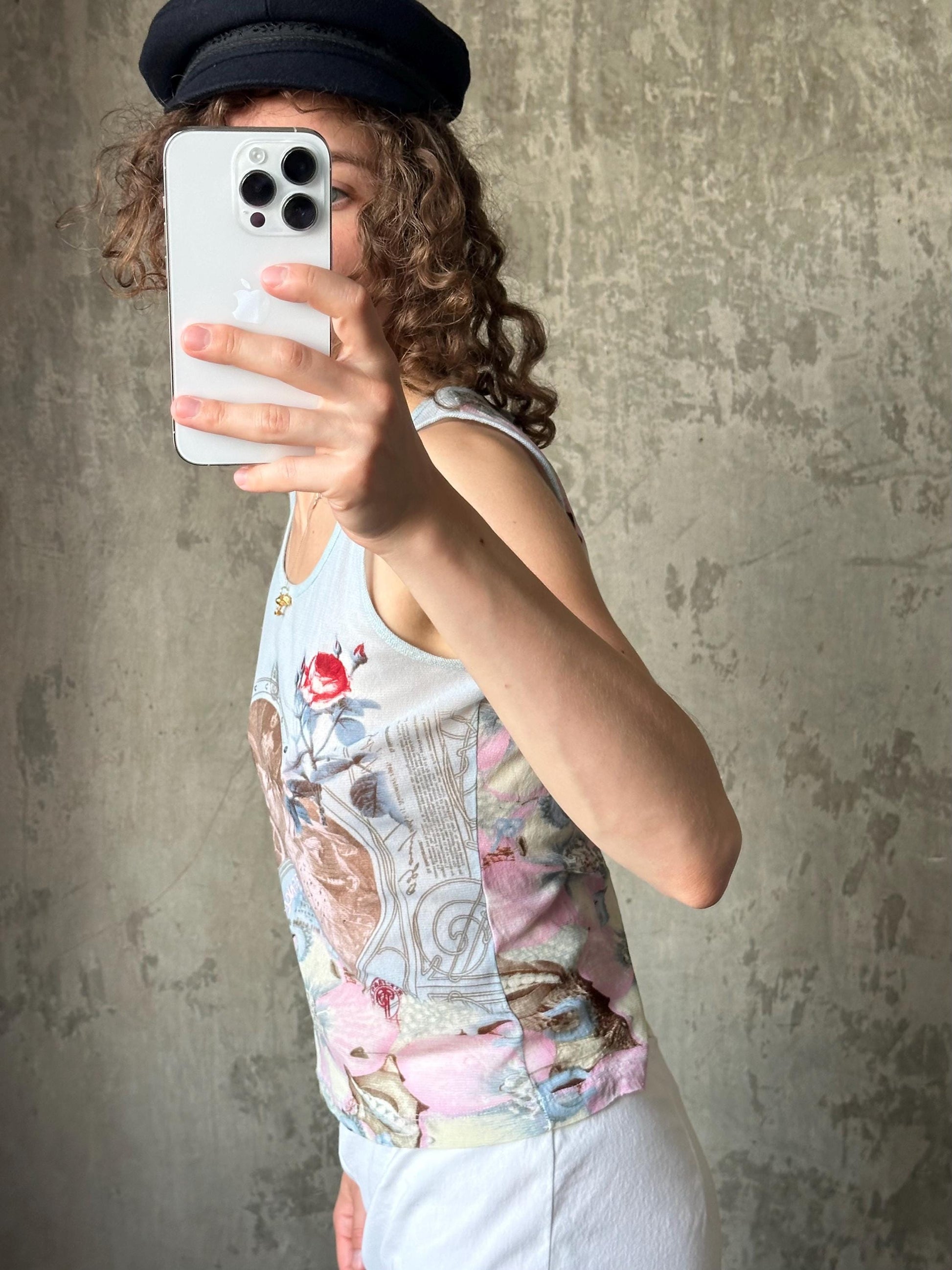 A person is taking a selfie with a smartphone, wearing a hat and a tank top with a floral pattern.
