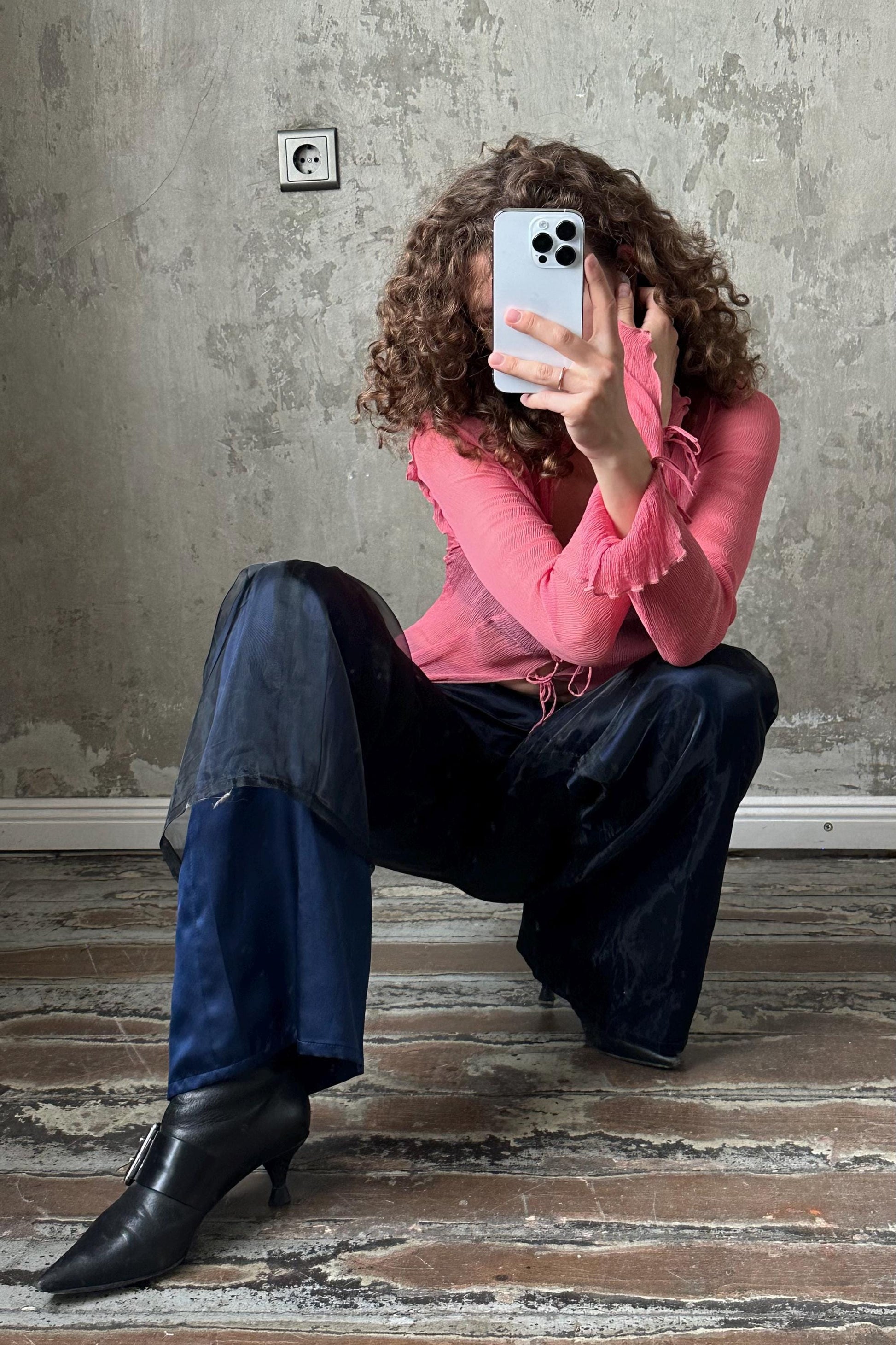 A person is sitting on the floor, taking a selfie with a smartphone.