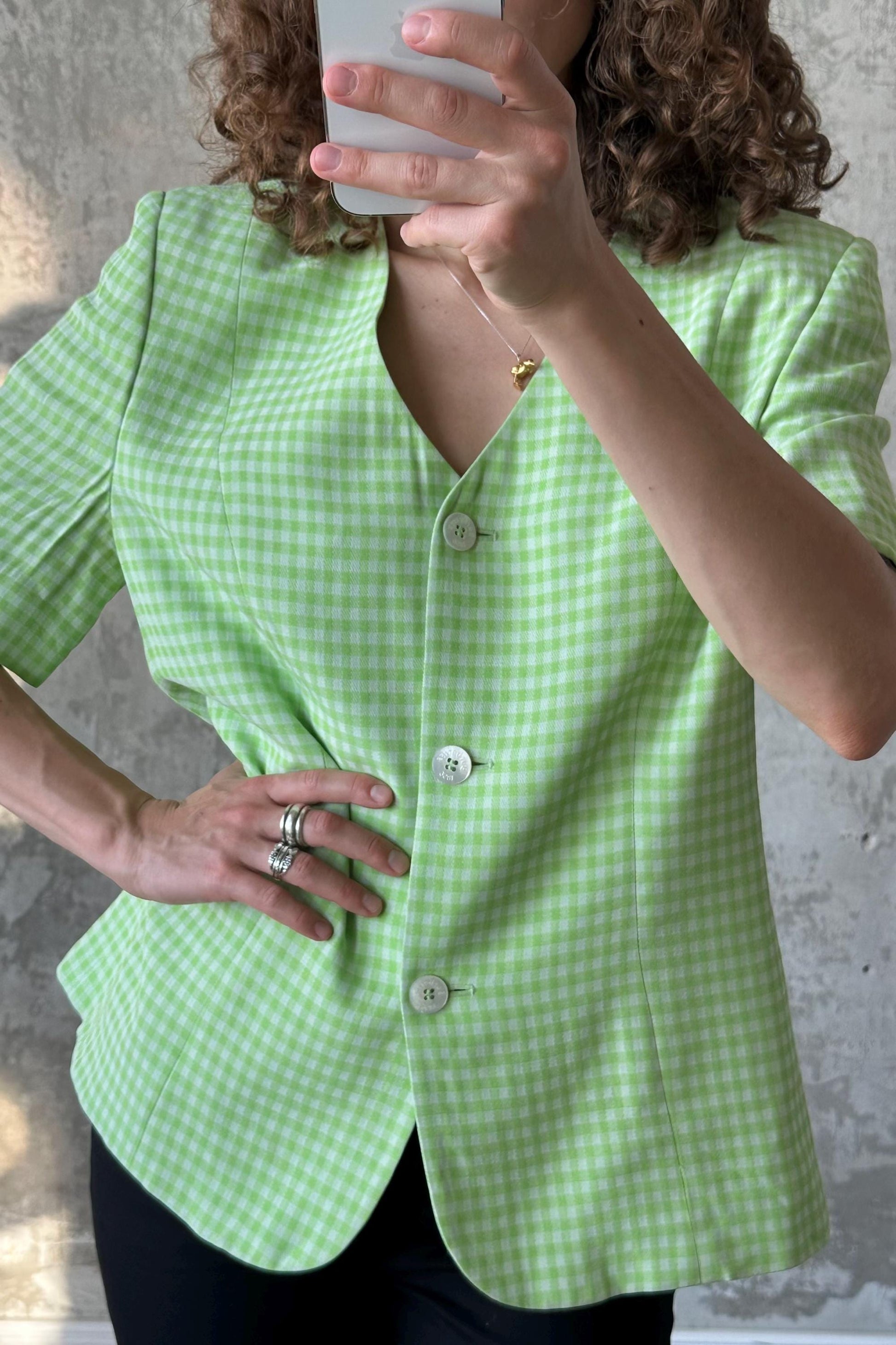 A person is taking a selfie with a green and white checkered blazer, wearing a ring and holding a phone.