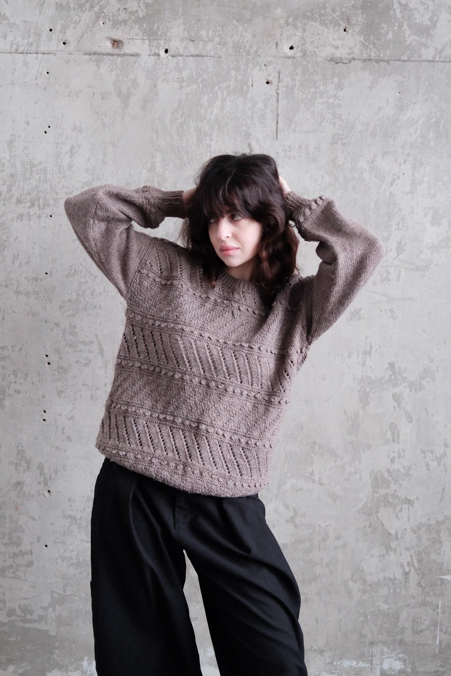 A person wearing a gray sweater is lying on the floor with their head resting on their hands, appearing relaxed and at ease.