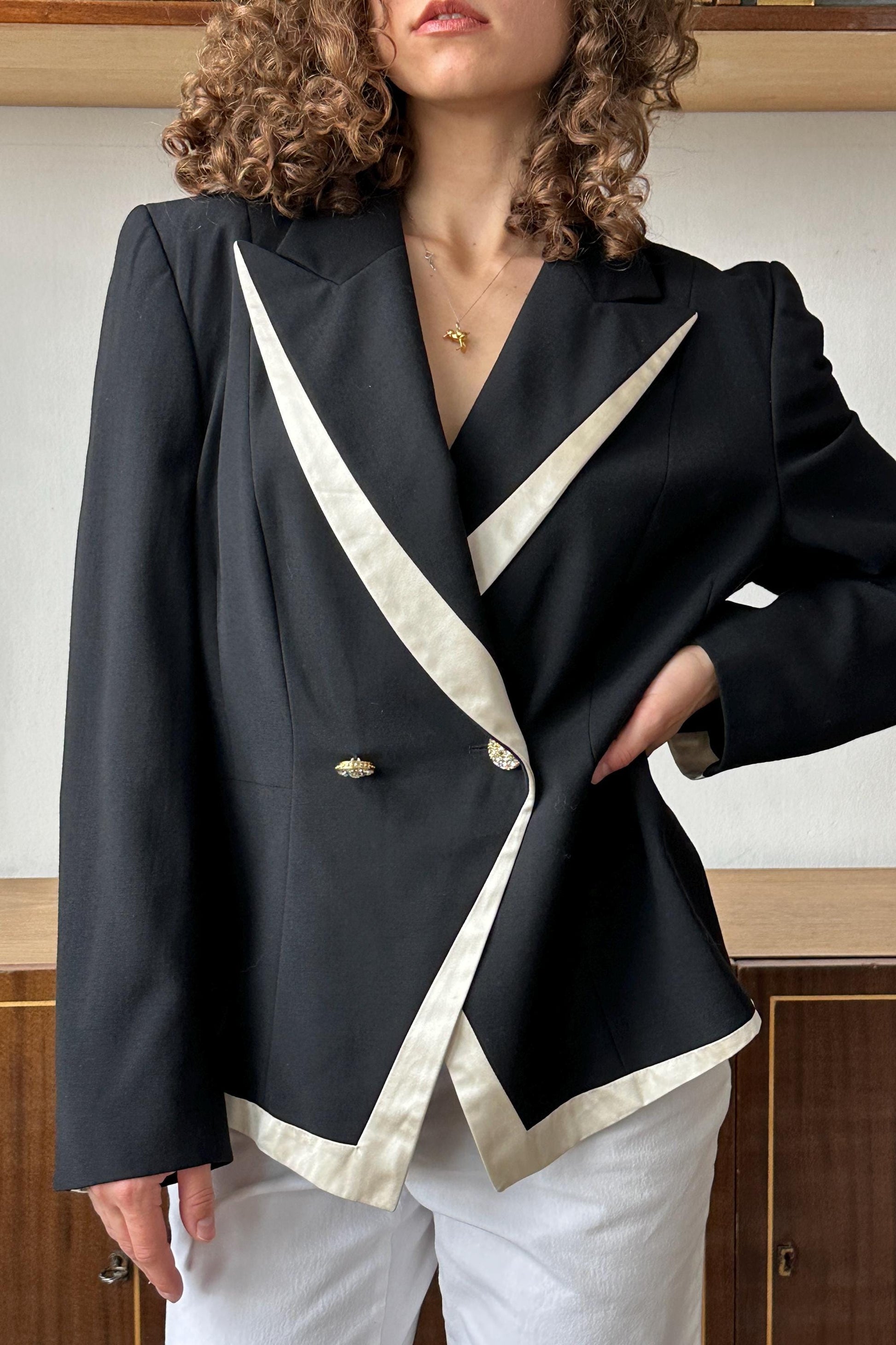 A woman wearing a black and white jacket with a white trim, posing in front of a wooden cabinet.
