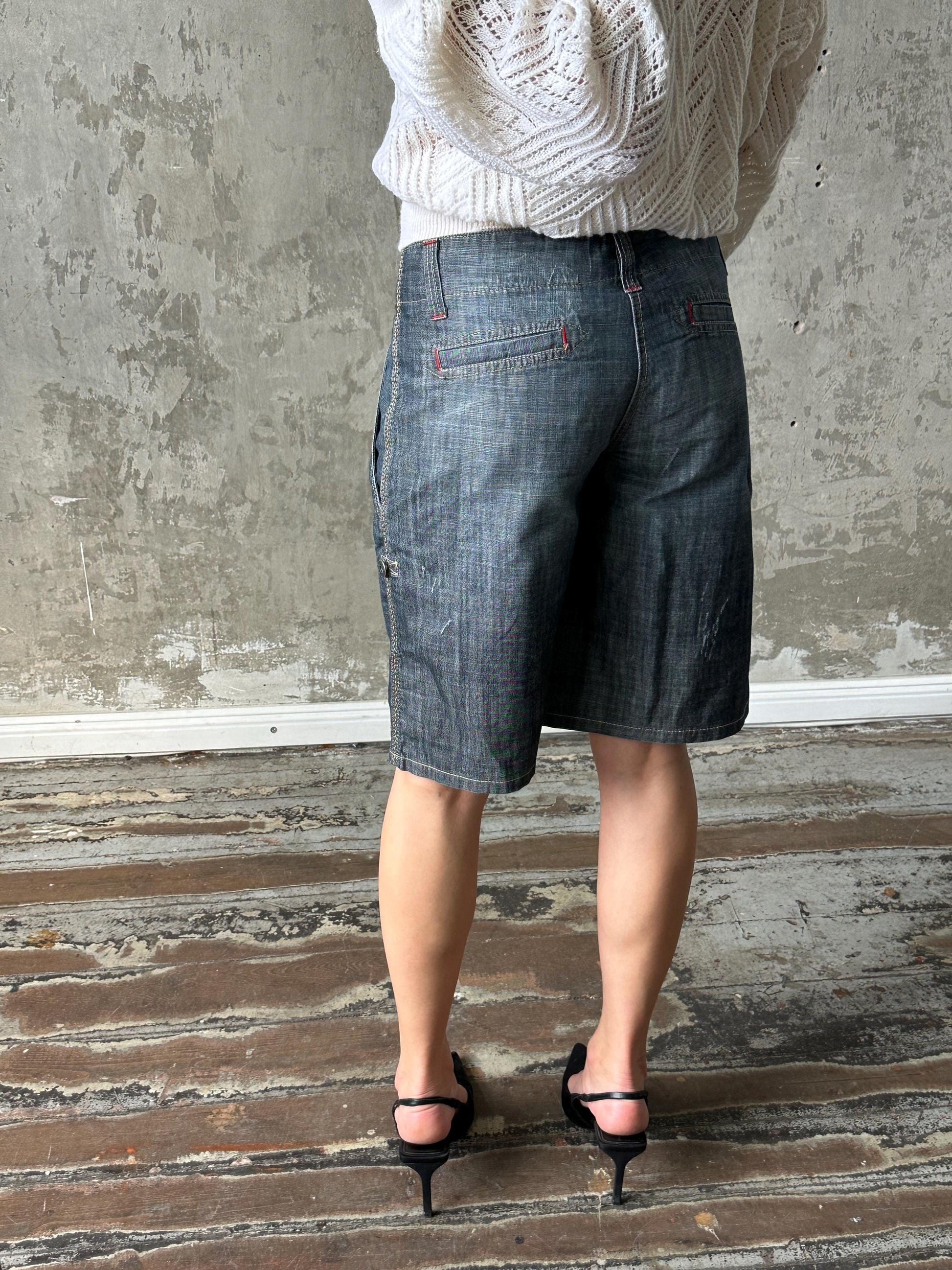 A person wearing a white sweater and black high heels stands in front of a concrete wall.