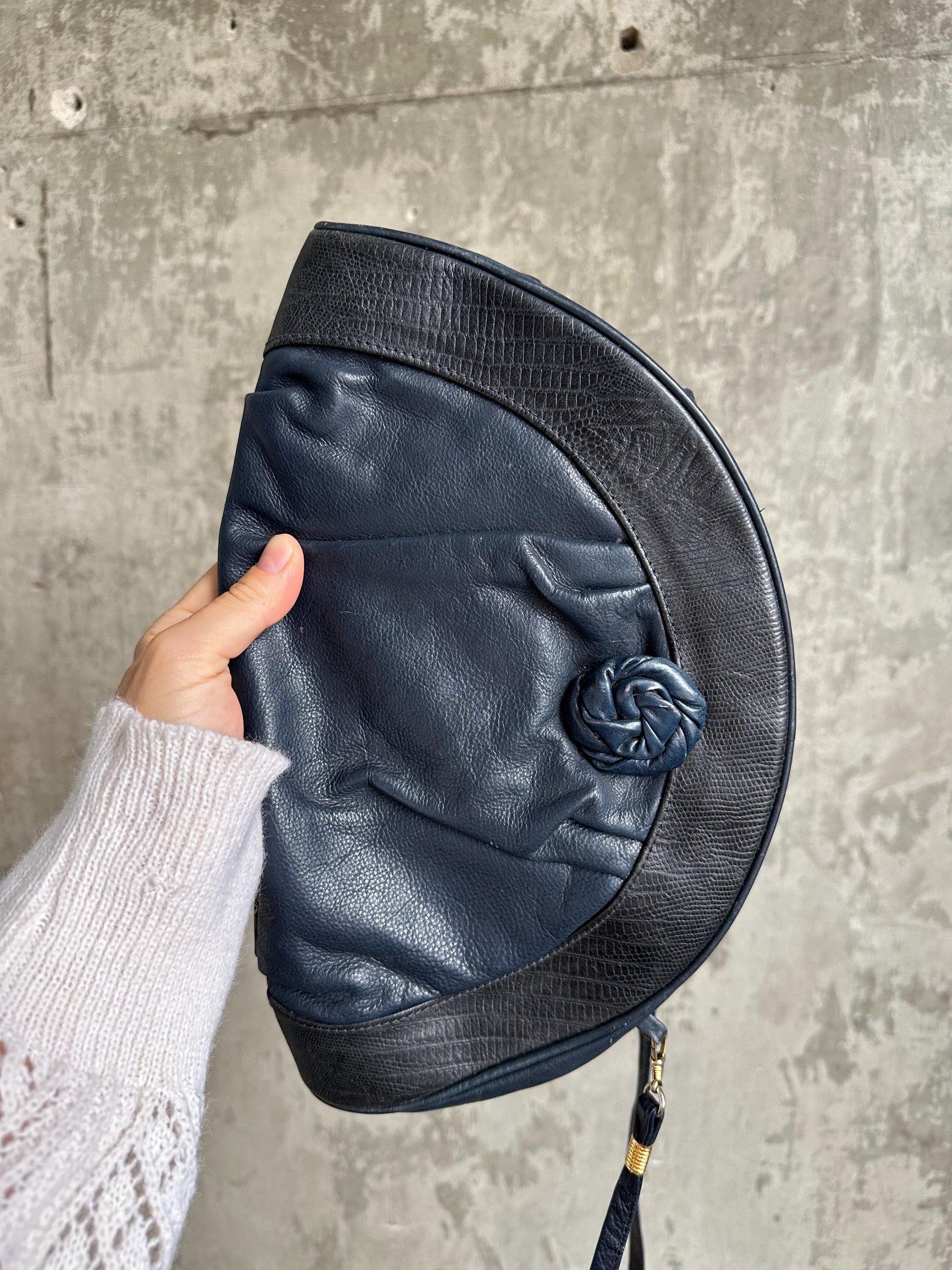 A hand holding a black leather purse with a twisted metal clasp.