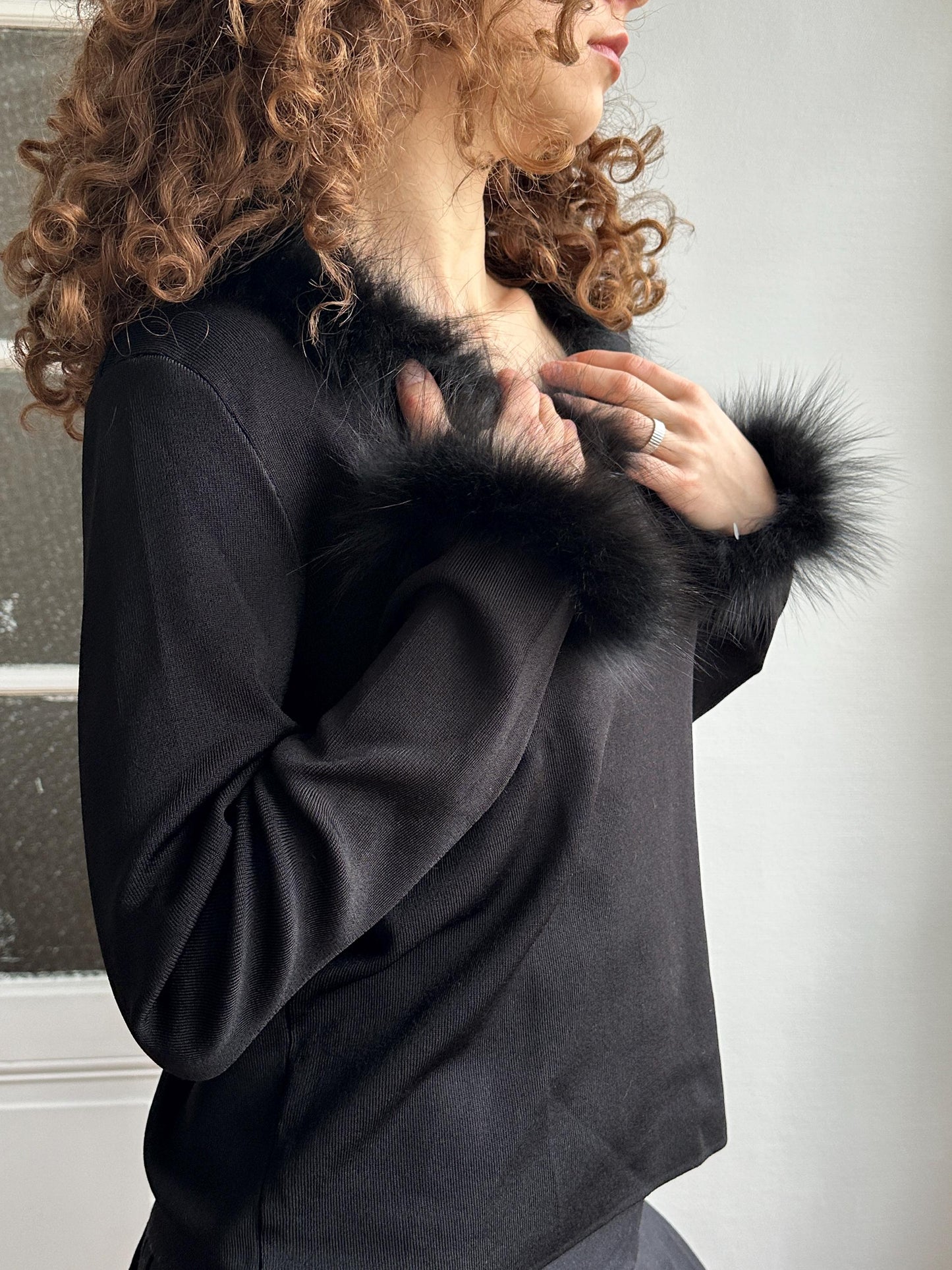A person with curly hair wearing a black fur coat is lying down and looking up.