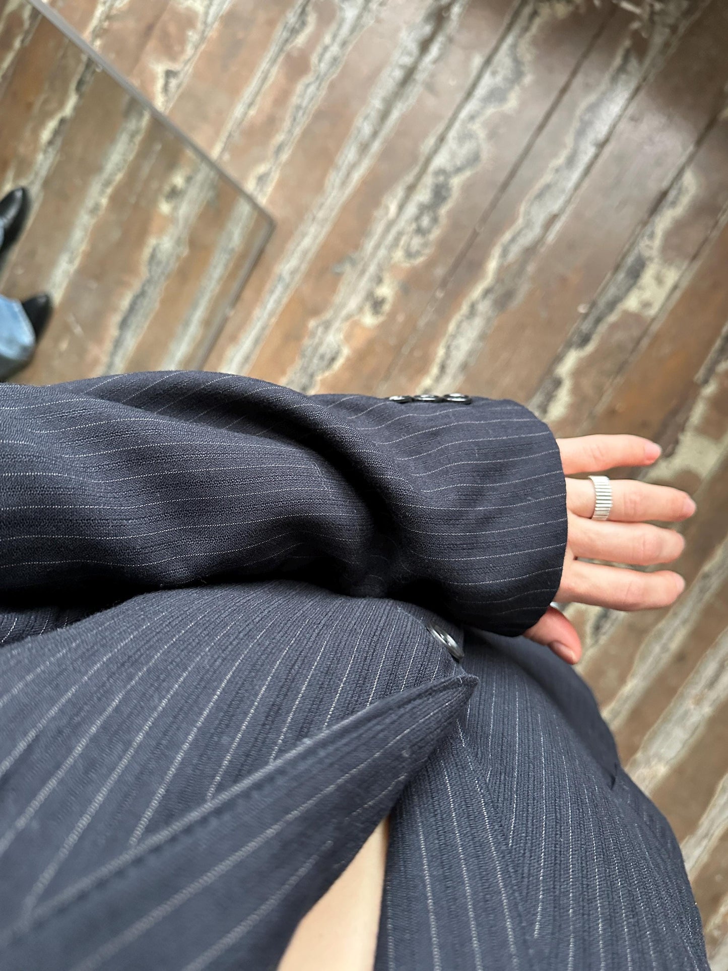 A close-up view of a person's hand wearing a pinstriped suit jacket, with a ring visible on the finger.