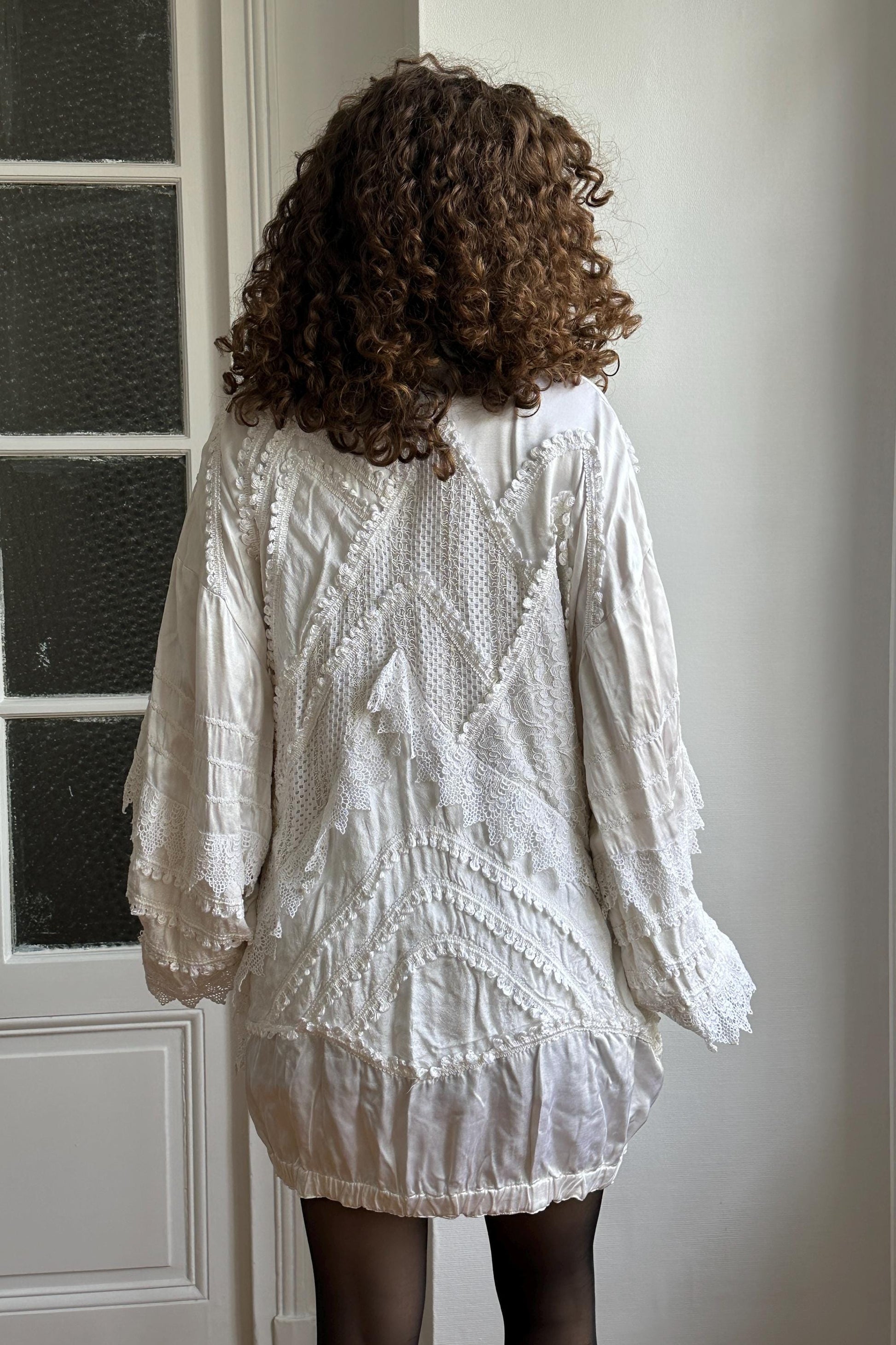 a person with curly hair wearing a white dress with intricate lace patterns and designs.