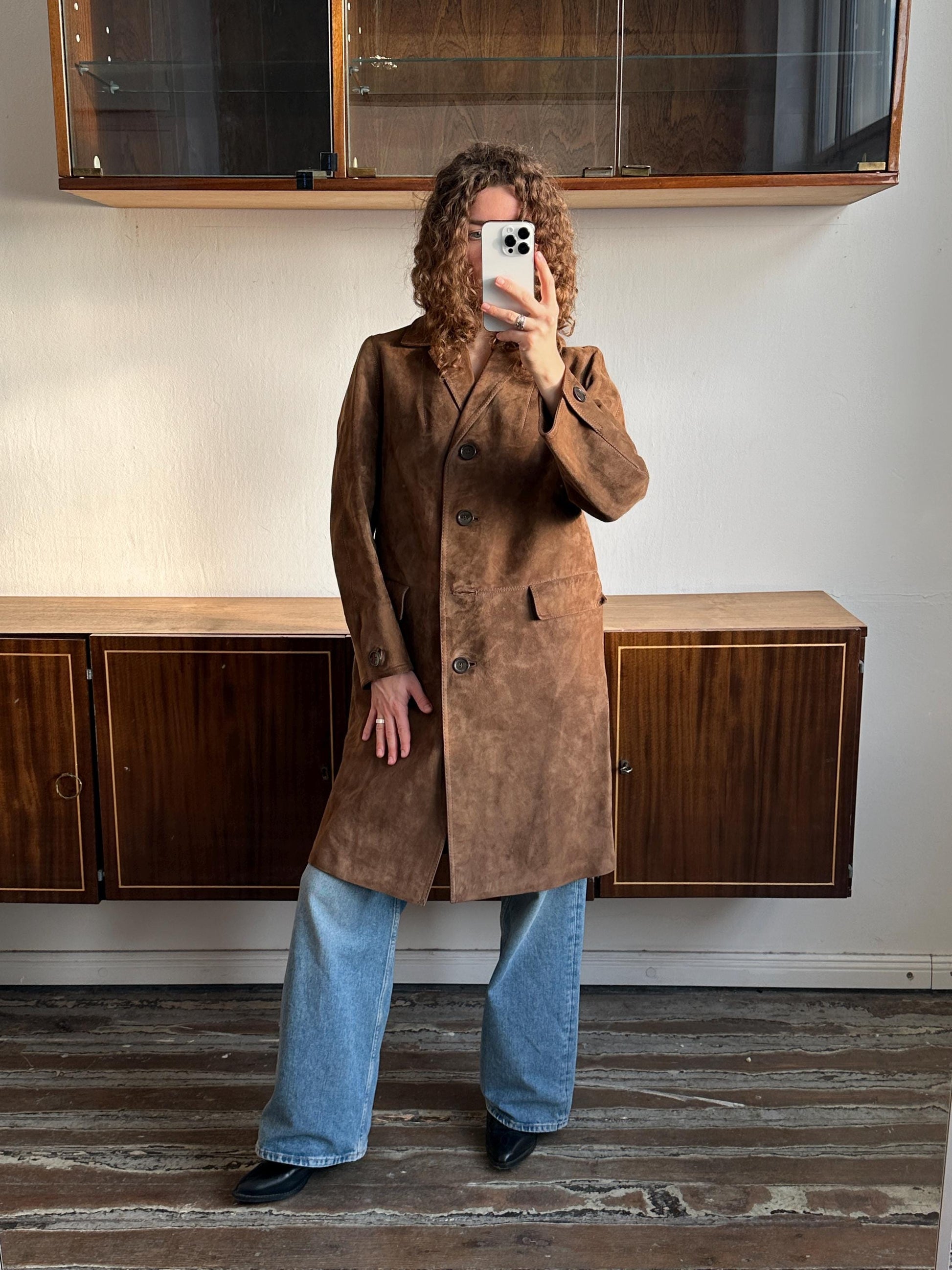 A person is taking a selfie in a room with wooden furniture, including a dresser and a cabinet.