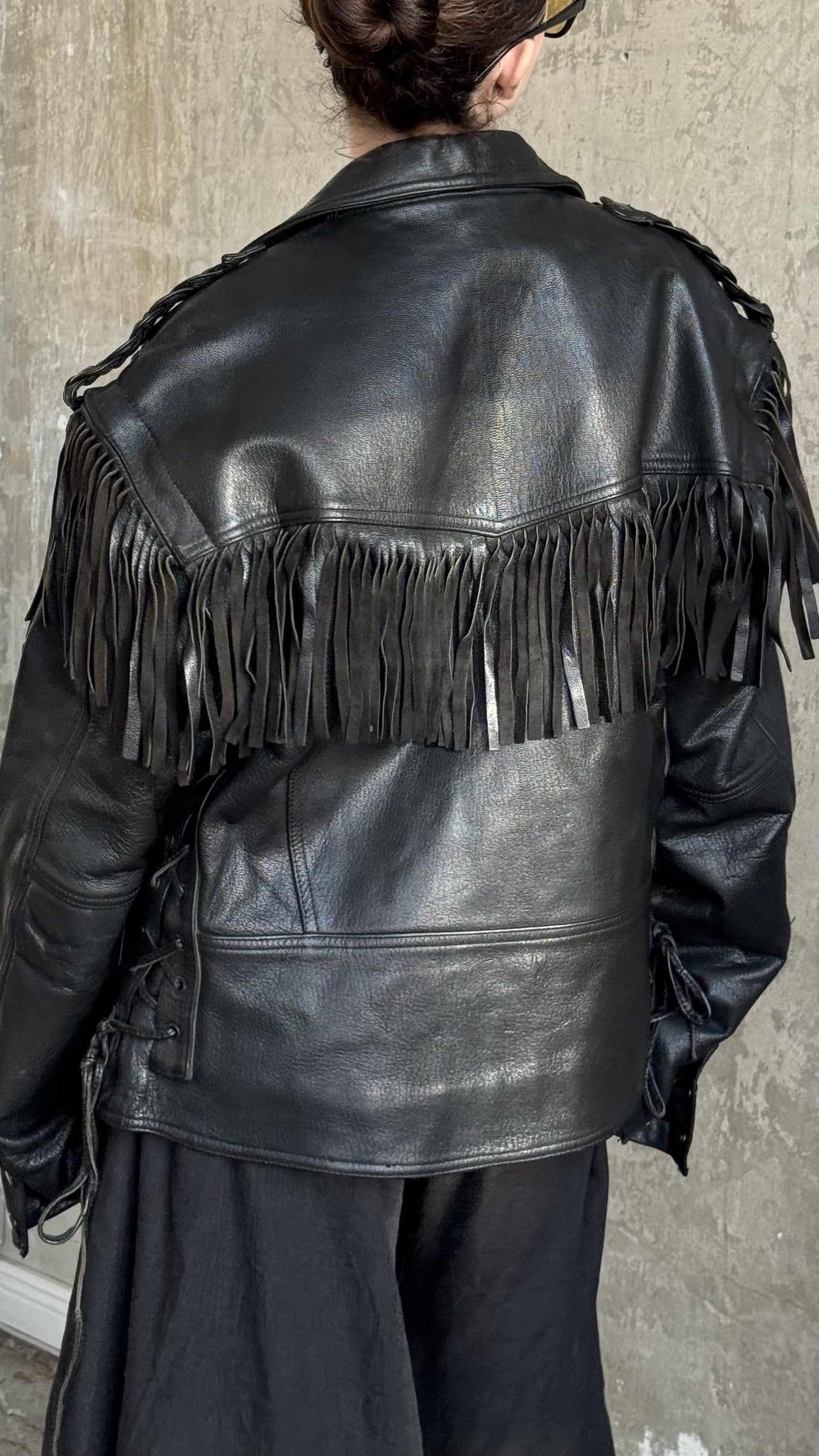 A person wearing a black leather jacket with fringe details.