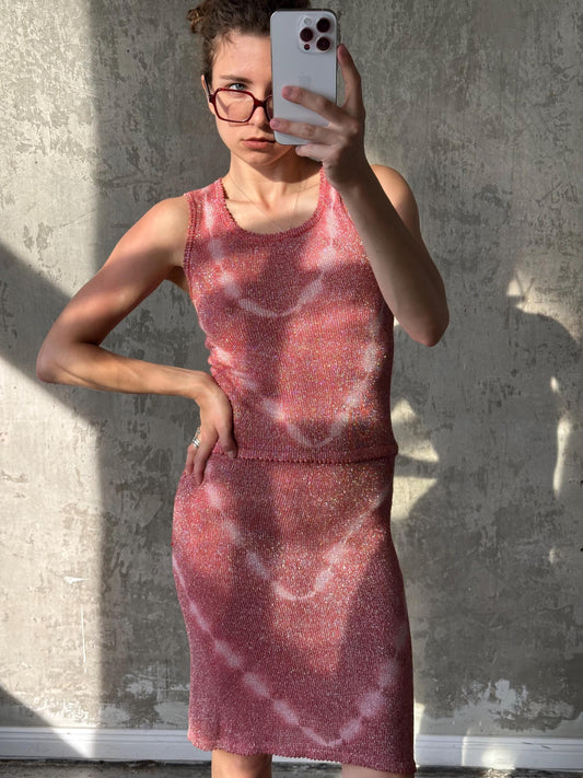 A woman wearing a pink dress is taking a selfie with a smartphone, standing in front of a concrete wall.