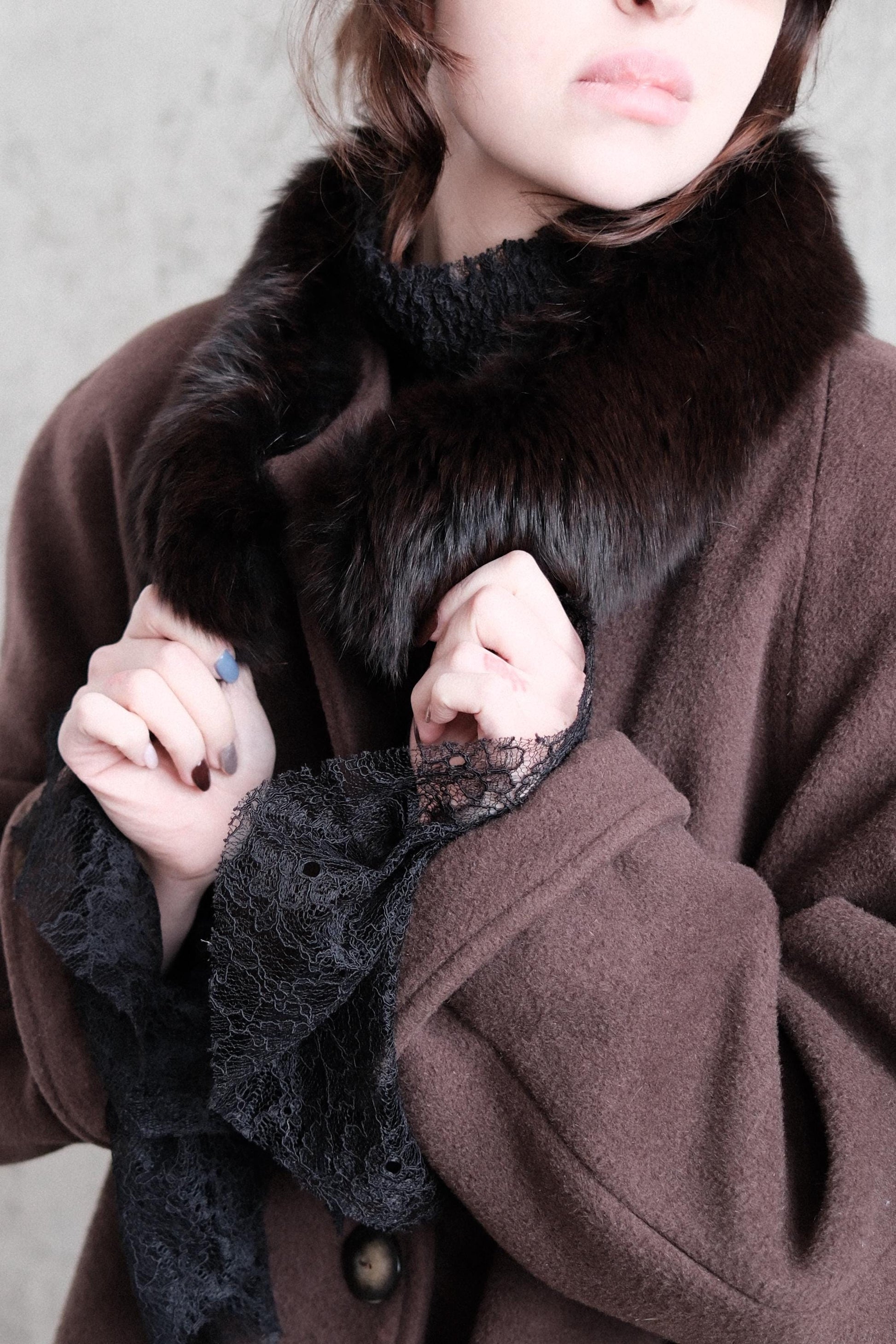A close-up view of a person's hand wearing a brown coat with lace trim, and a fur collar.