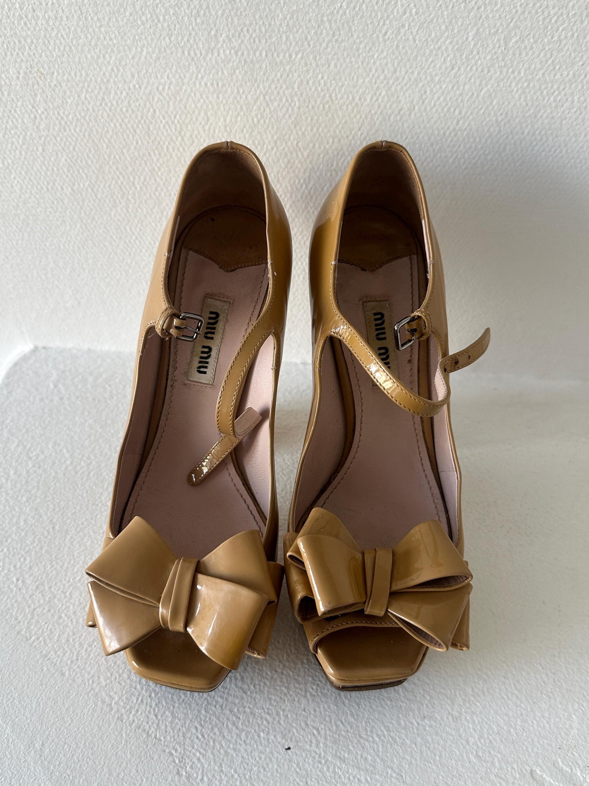 A pair of tan high-heeled shoes with bows on the toe and heel.