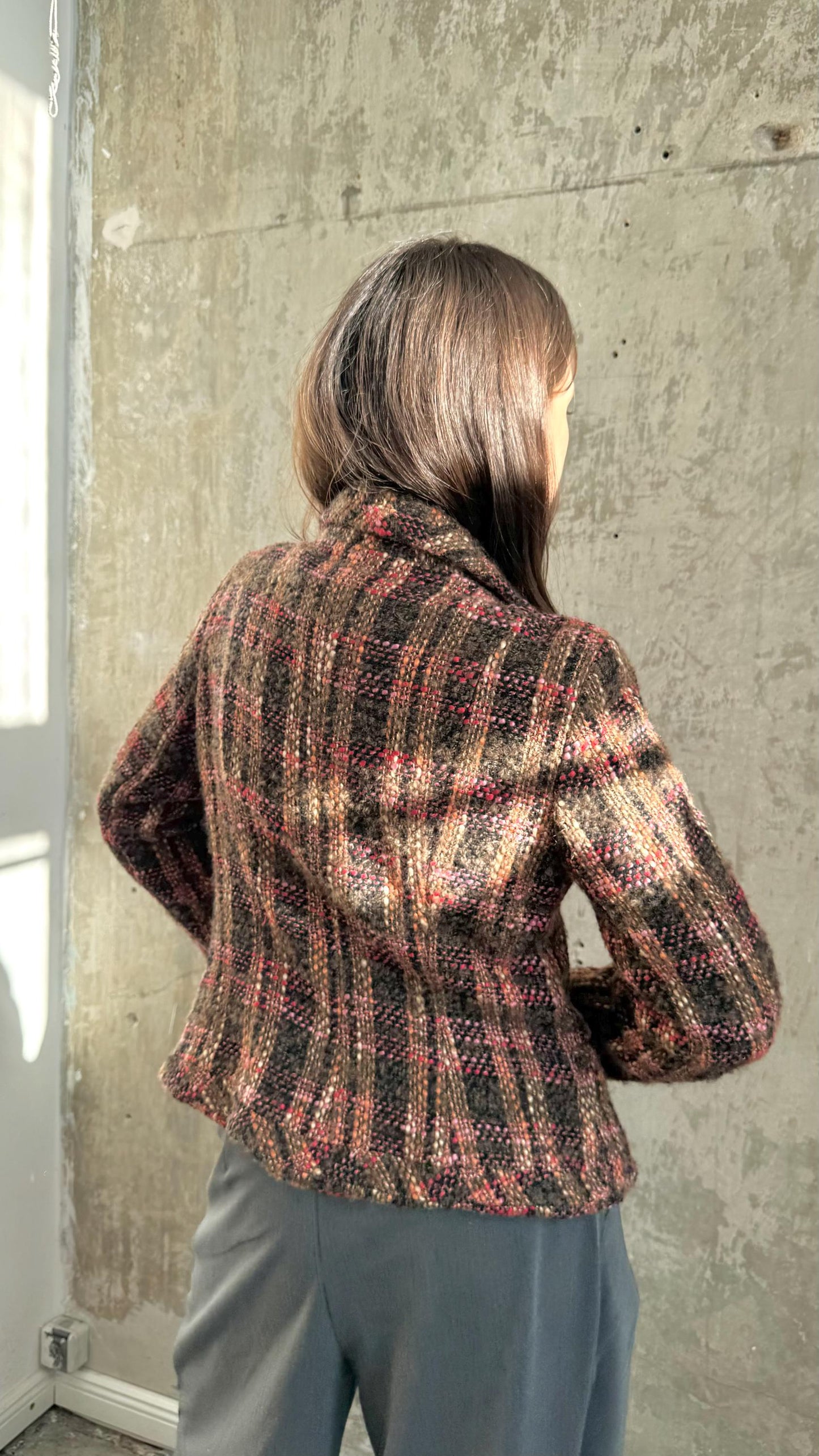a person standing in front of a concrete wall, wearing a plaid jacket.