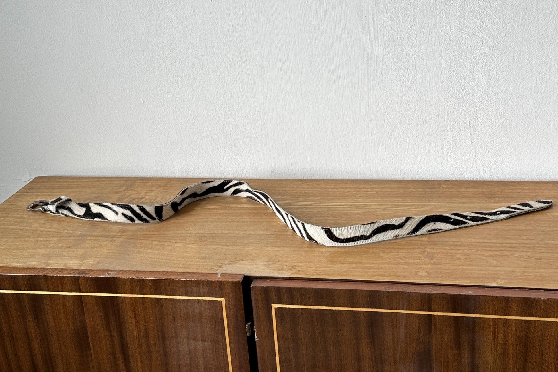 A zebra-striped belt is lying on a wooden surface, possibly a cabinet or dresser.