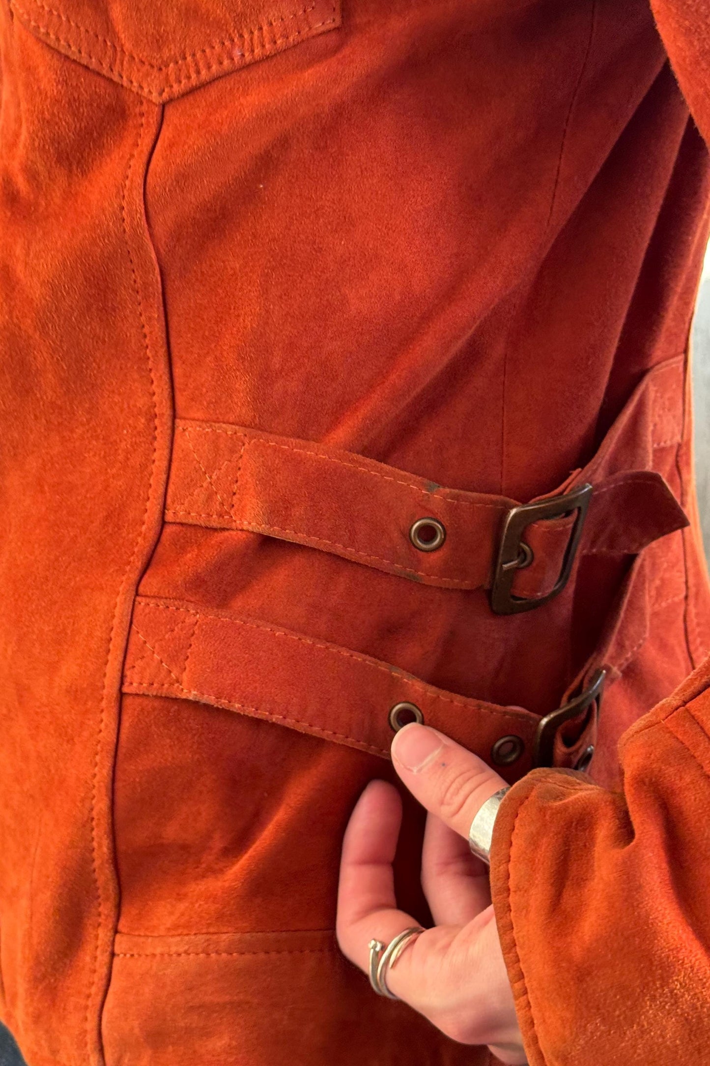 A close-up view of a person's hand wearing a red leather jacket with a buckle detail.