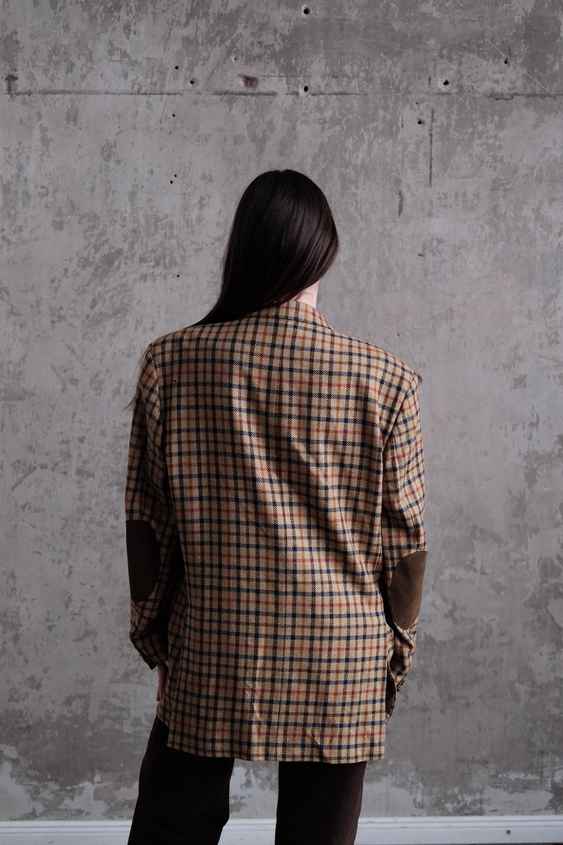 a person wearing a plaid jacket standing against a concrete wall.