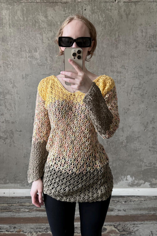 A person is taking a selfie with a smartphone, wearing a colorful, crocheted sweater and sunglasses.