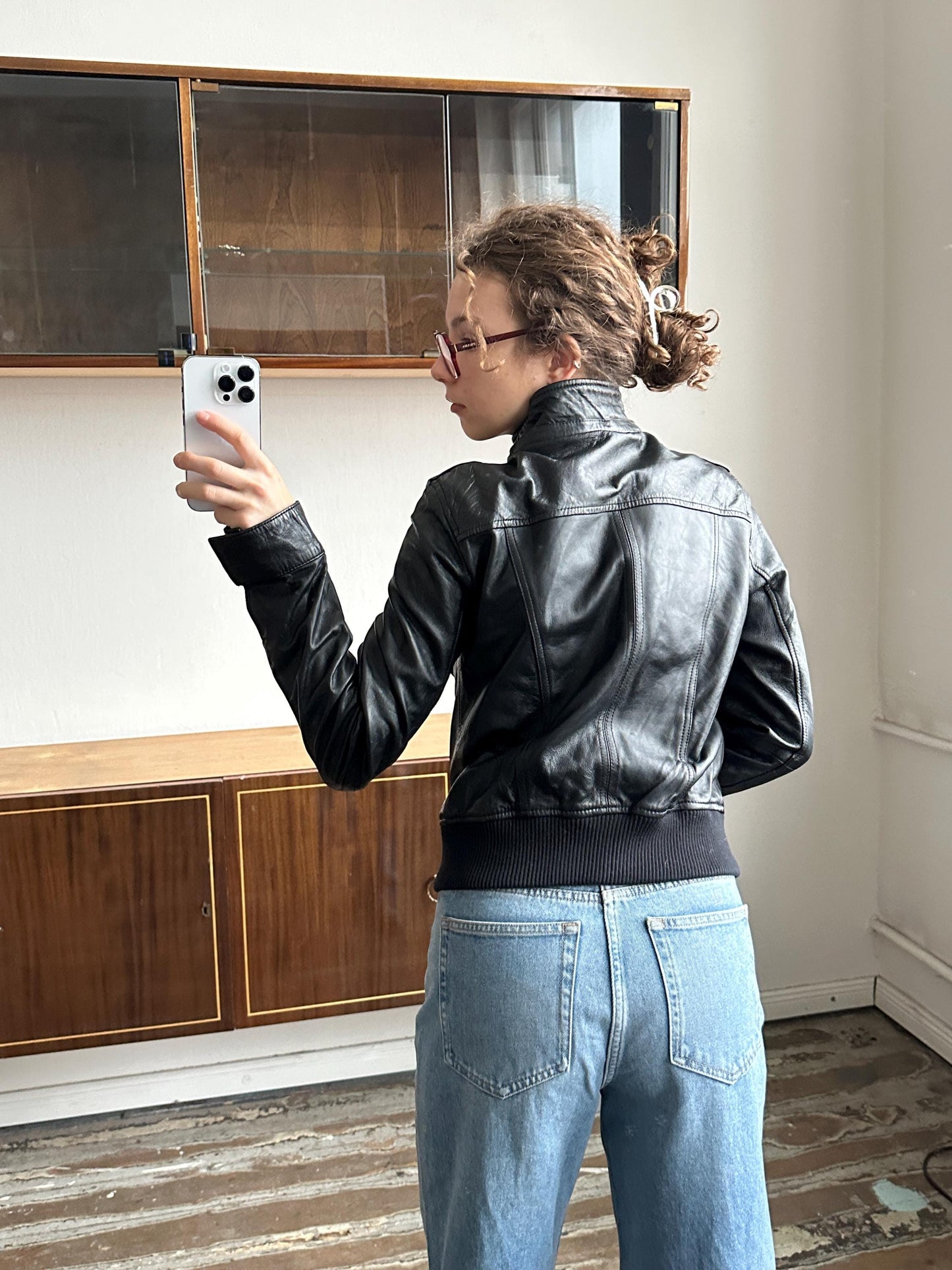 A person is taking a selfie in a room with a wooden floor and a glass door.