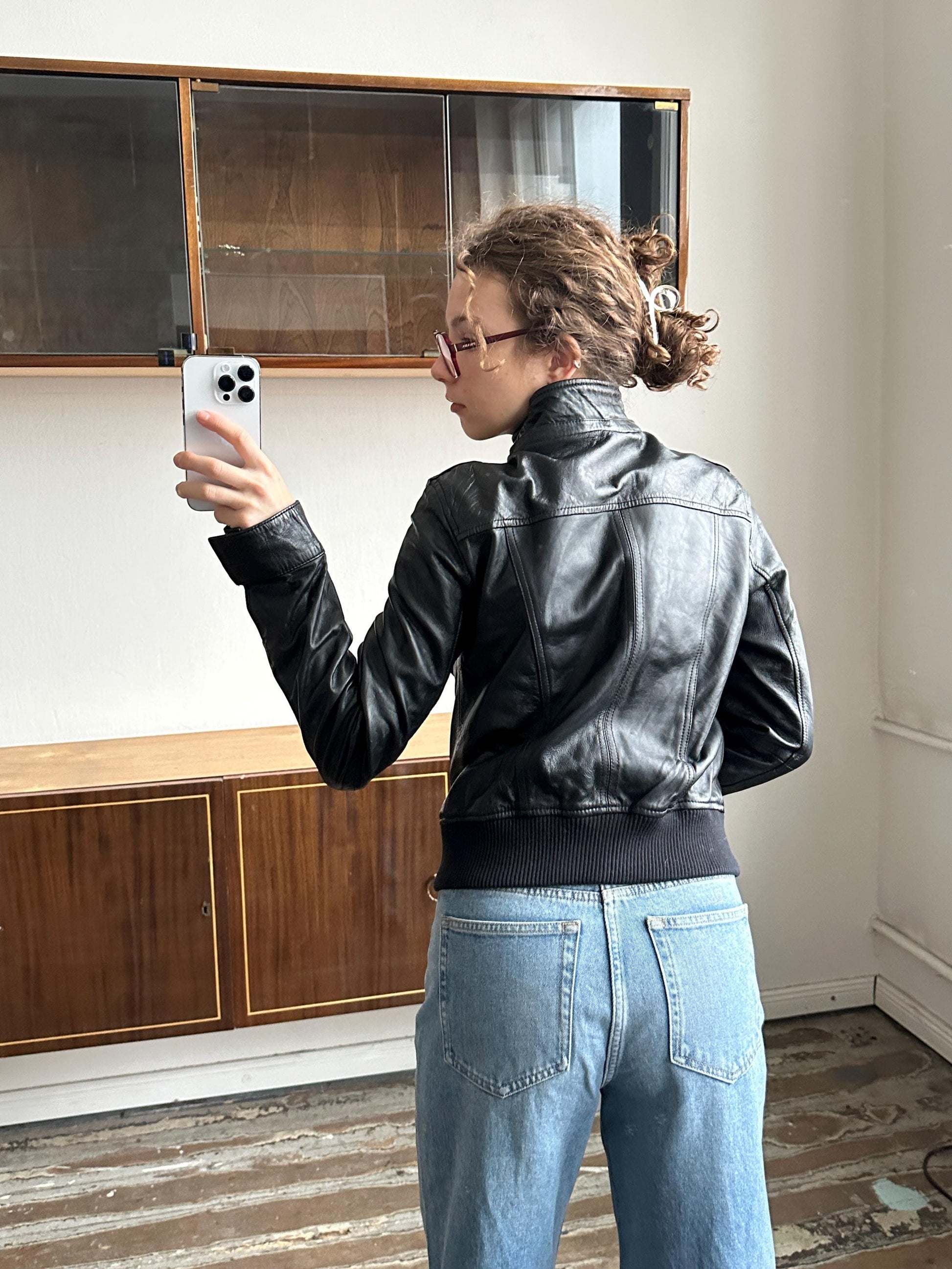 A person is taking a selfie in a room with a wooden floor and a glass door.