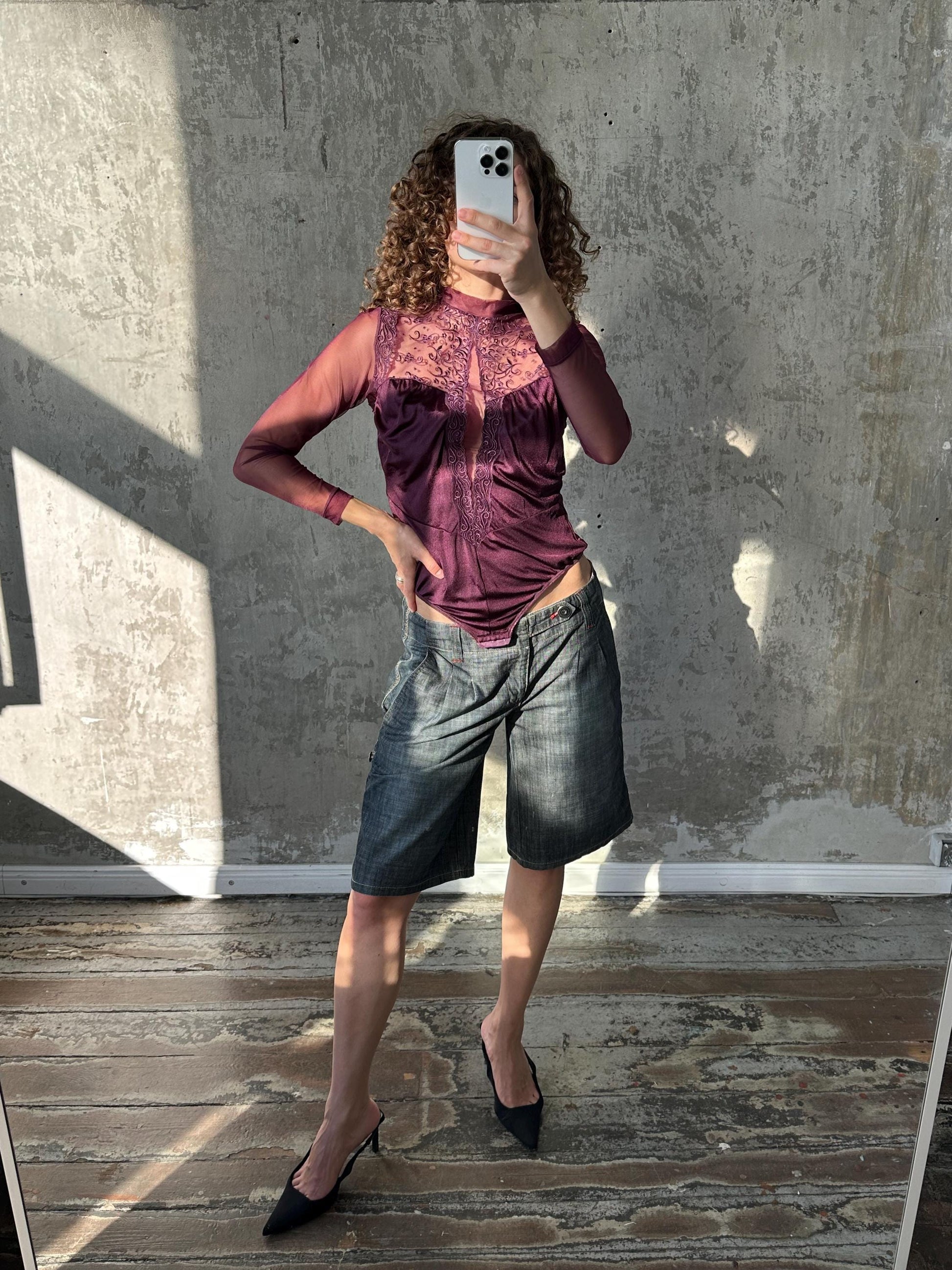 A woman is taking a selfie in front of a concrete wall, holding a smartphone in her hand.