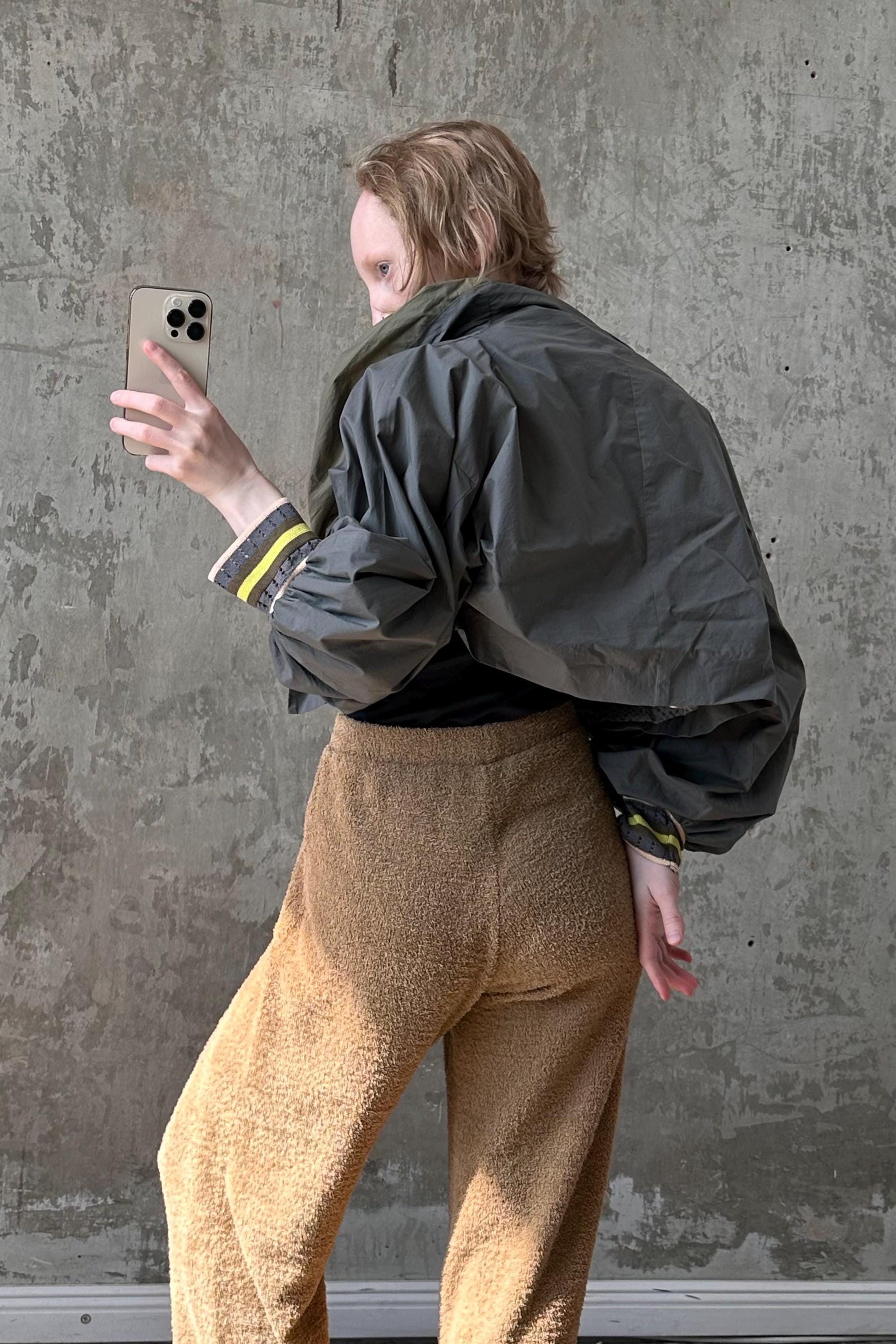 a woman standing in front of a concrete wall holding a cell phone