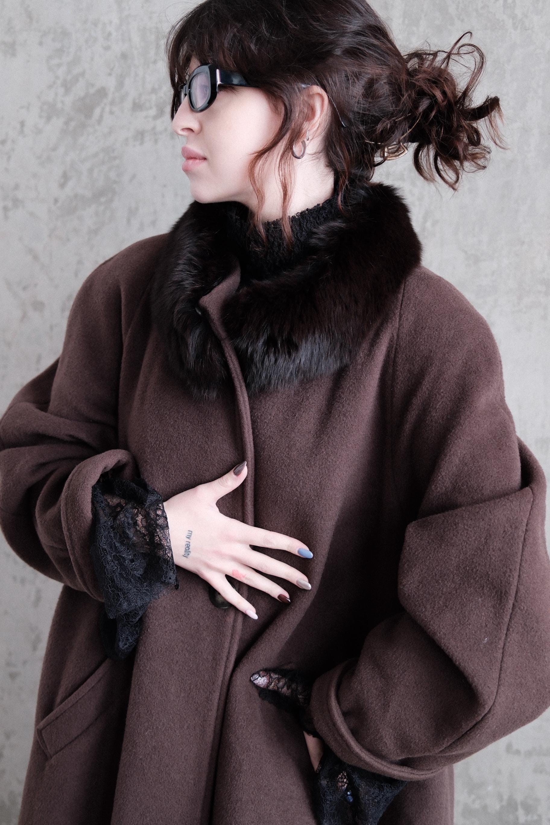 A woman wearing a brown coat and sunglasses is lying down on a concrete floor.