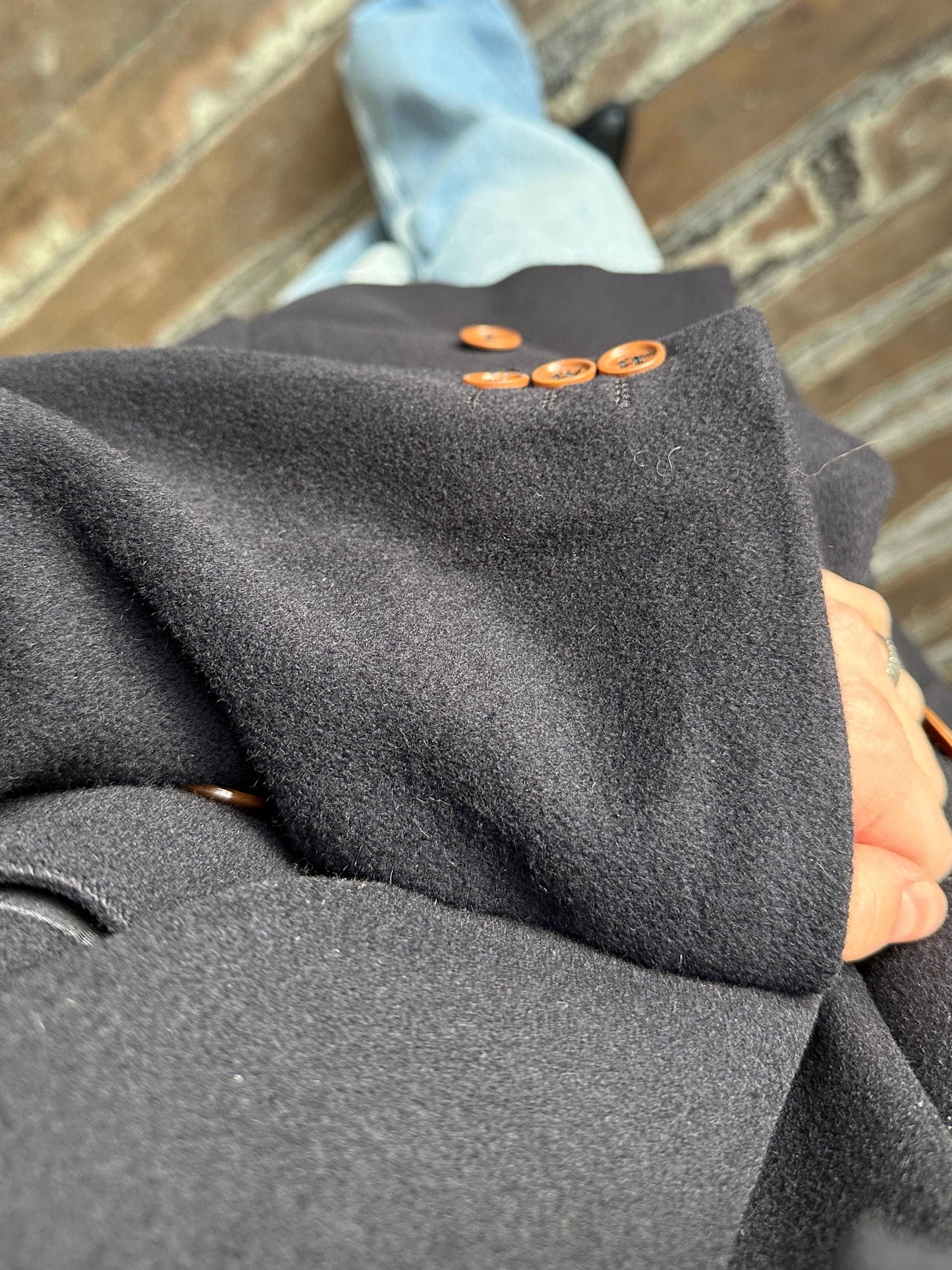 A close-up view of a person's arm wearing a dark gray coat with orange buttons, standing on a wooden floor.
