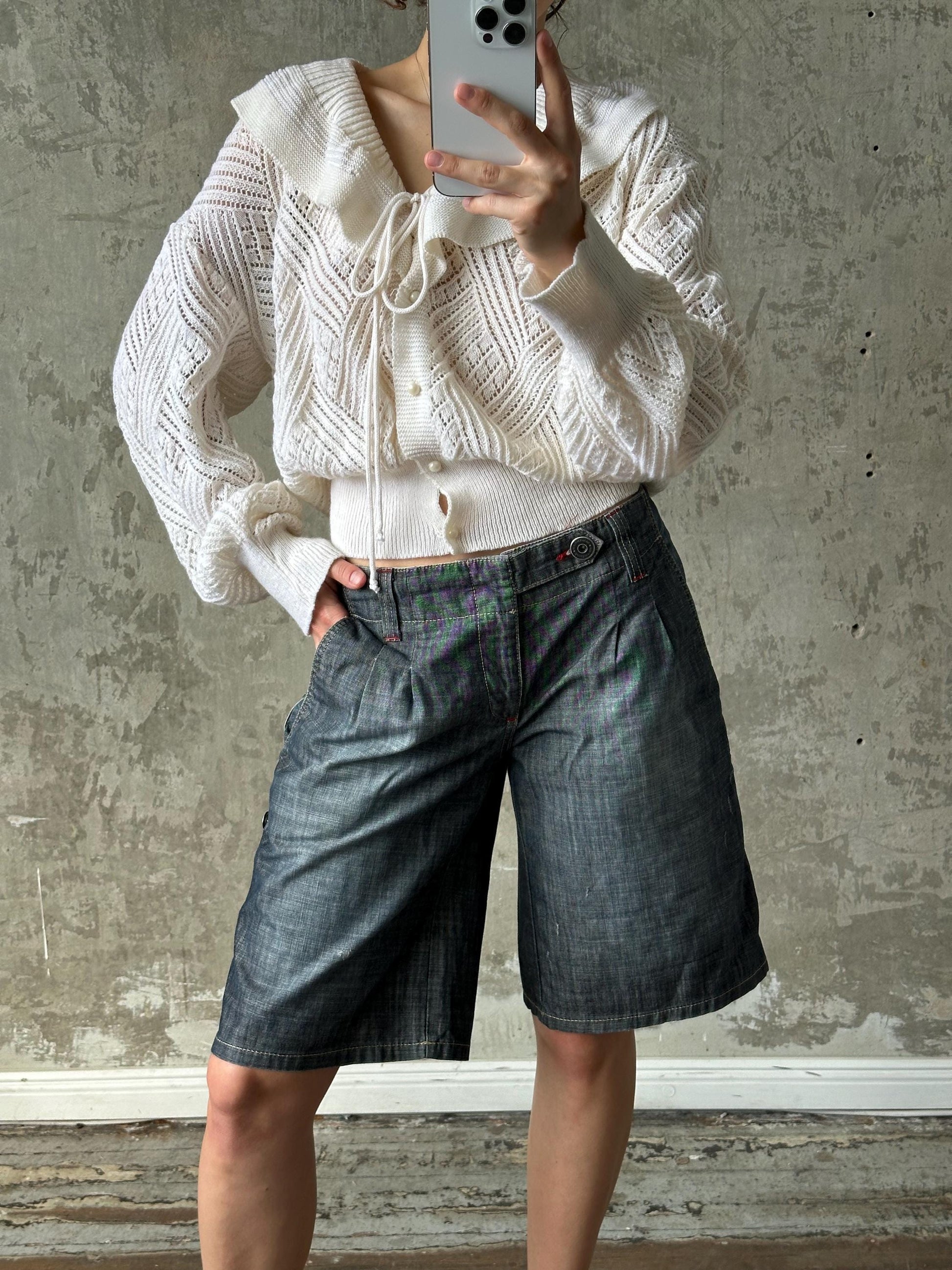A person is taking a selfie with a white sweater and blue jeans, holding a smartphone in their hand.