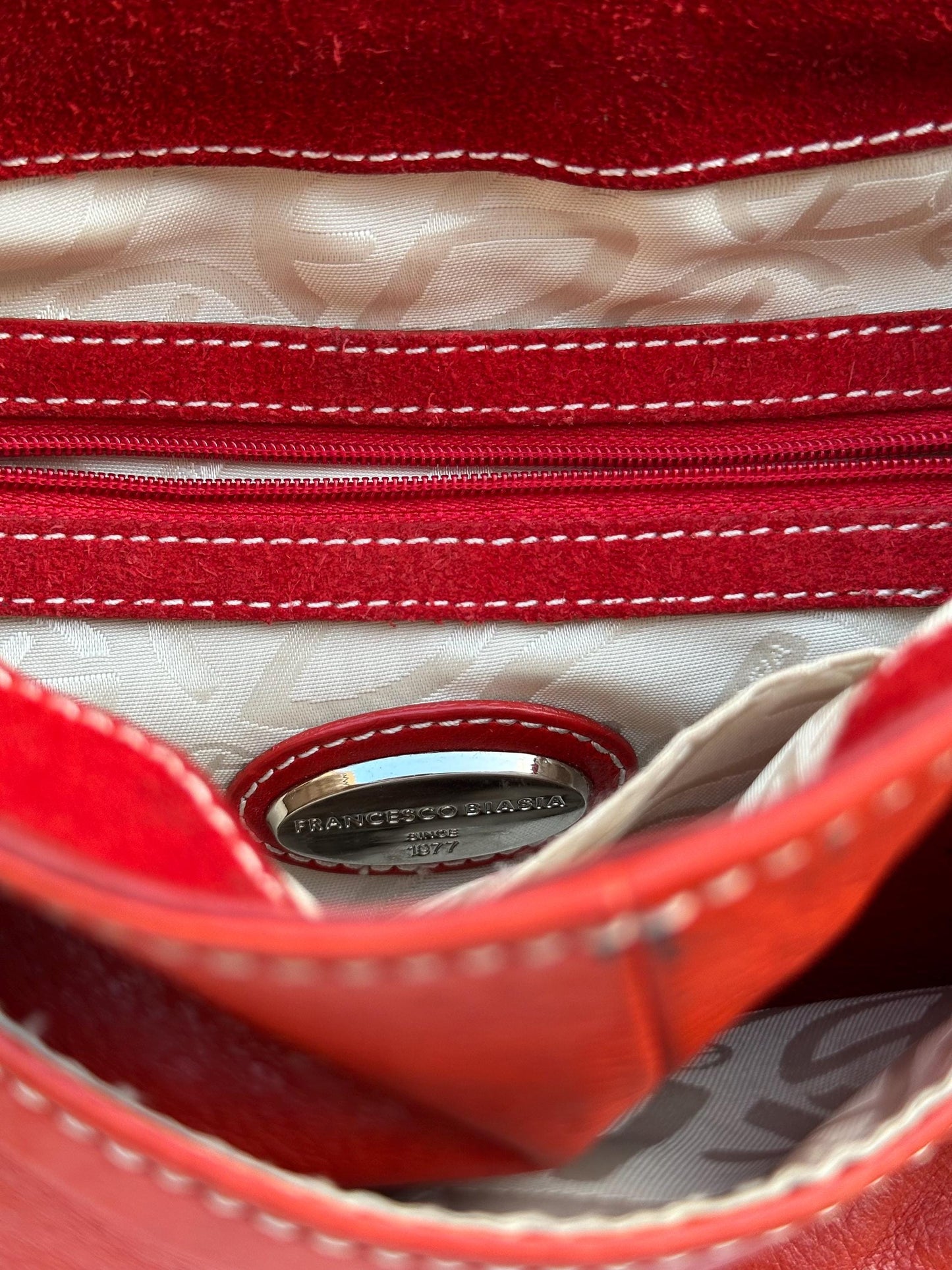 the interior of a red leather handbag, with a zipper and a small metal tag visible inside.