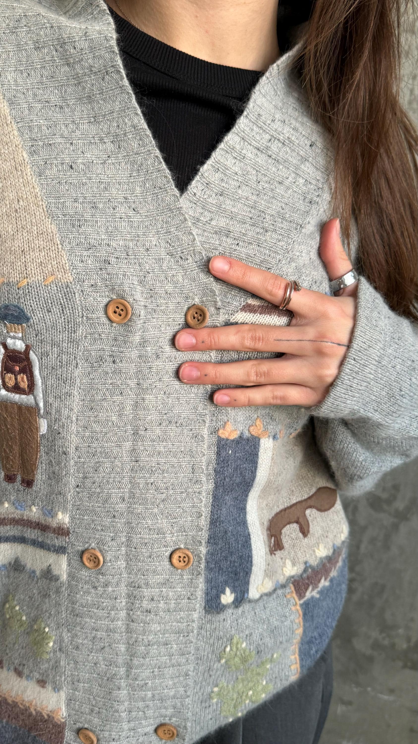 A close-up of a person wearing a gray cardigan with a pattern of animals and buttons.