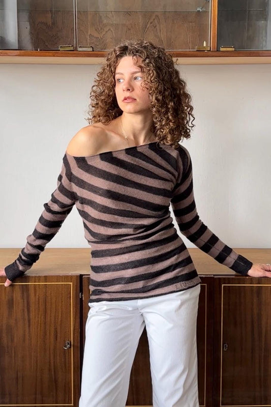 A woman with curly hair wearing a striped sweater stands in front of a wooden cabinet.