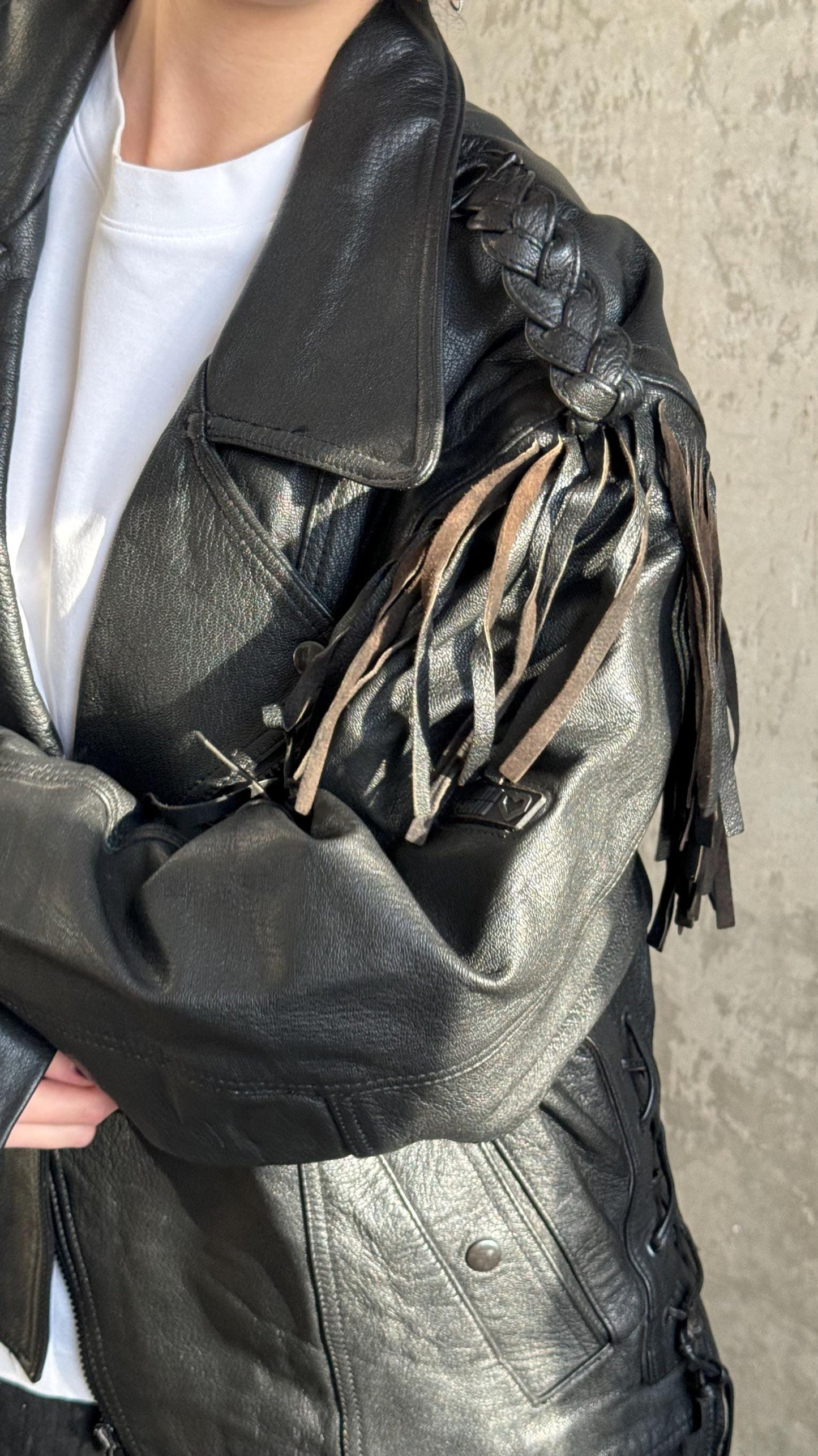 A close-up of a person wearing a black leather jacket with fringe details.