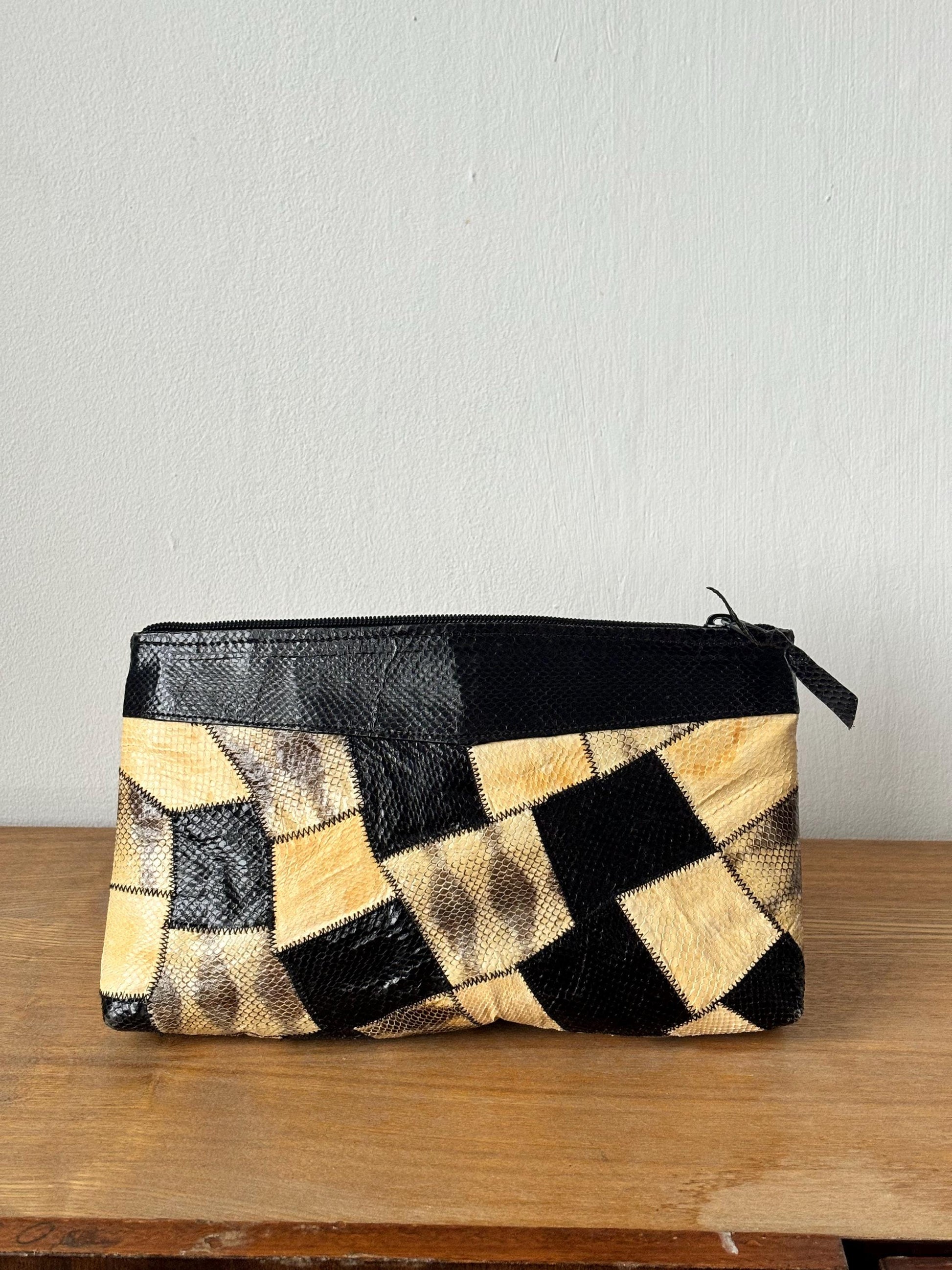 A black and beige patterned clutch purse is displayed on a wooden surface against a white wall.
