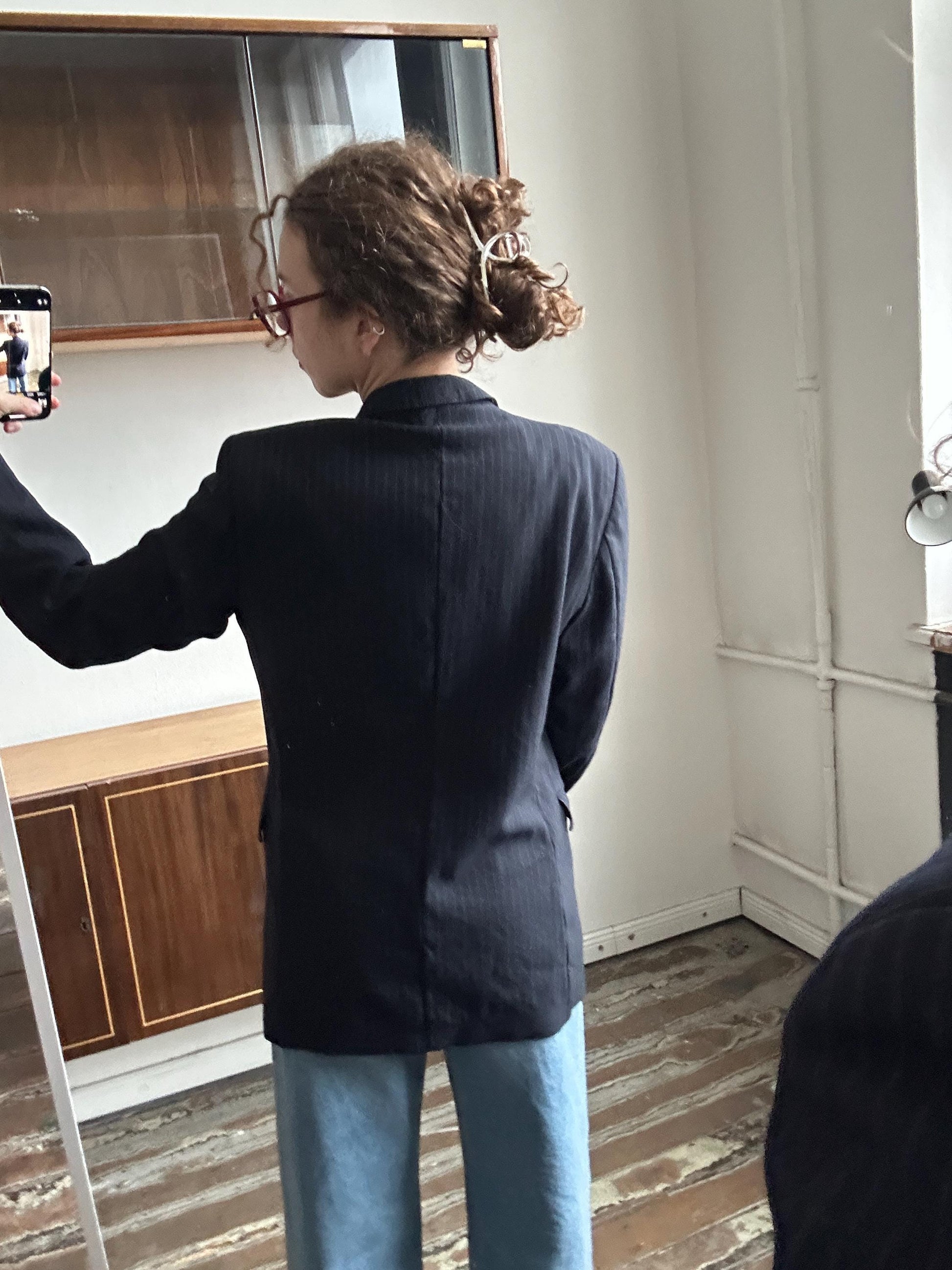 a person taking a selfie in a mirror, wearing a black jacket and blue pants.
